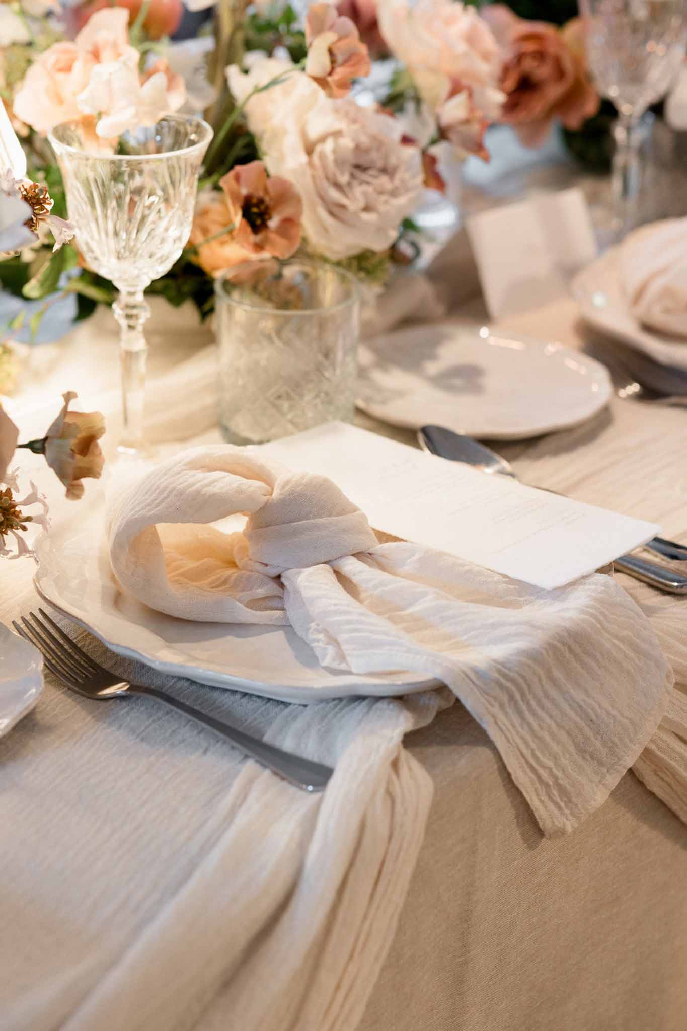 Wedding place setting with scallop-edged plate, cheesecloth napkin, menu card, and blush and terracotta floral centerpiece