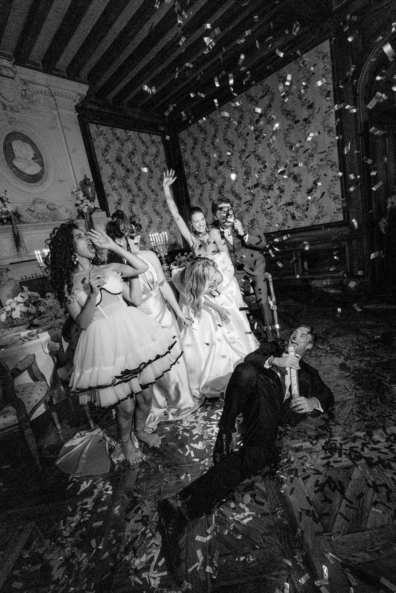 Black and white confetti cannon moment with masked guests in ornate chateau reception room