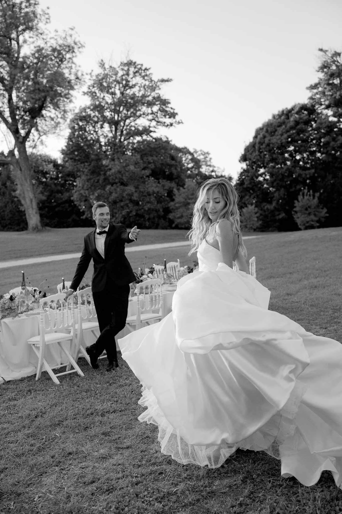 Black and white photo of bride and groom walking beside outdoor reception banquet table on lawn