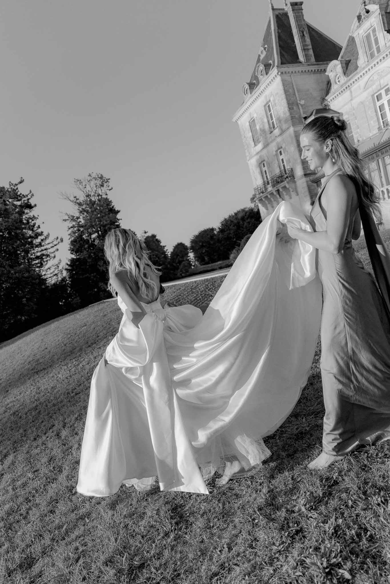 Black and white bridesmaid lifting satin gown train with bow detail on chateau lawn