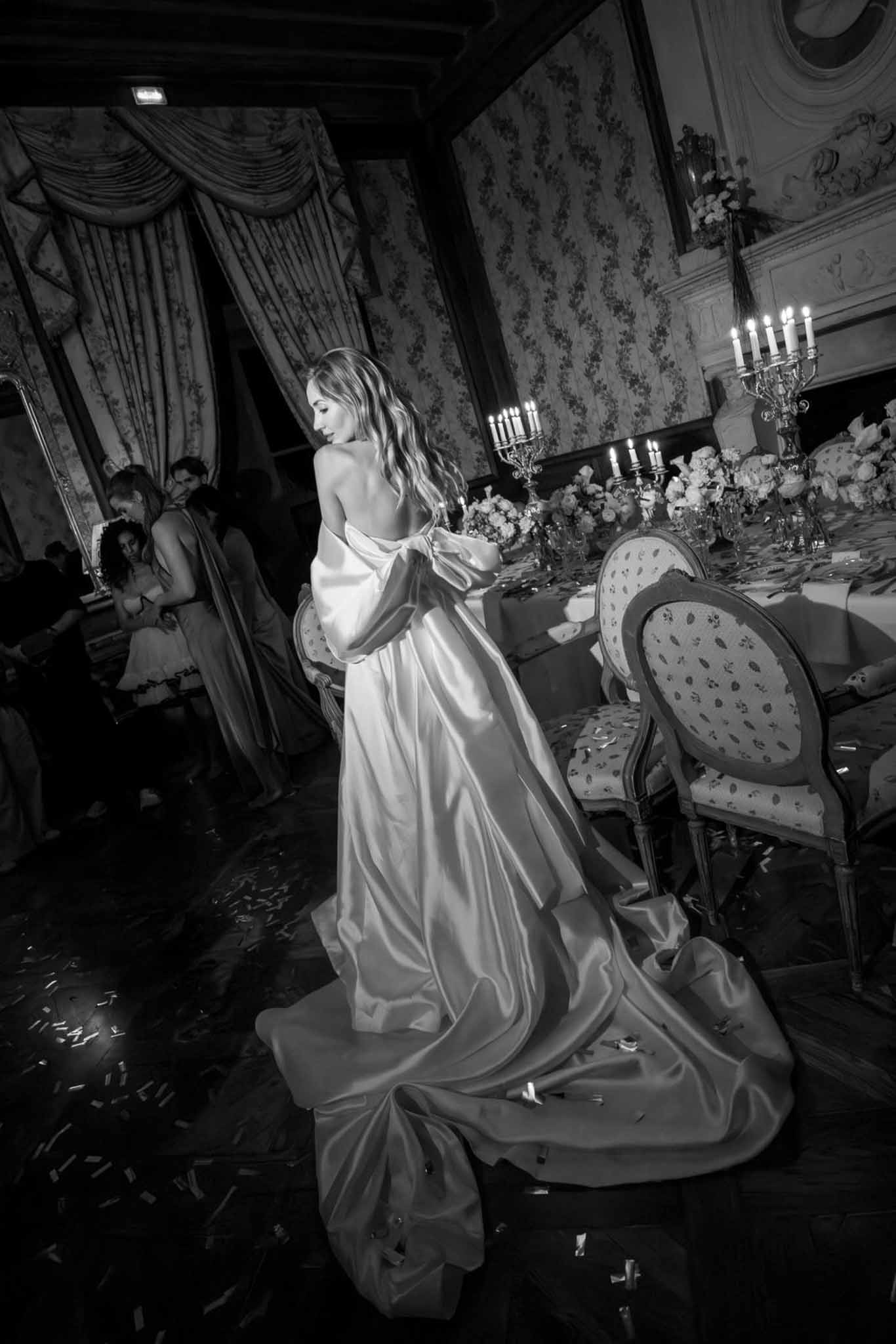 Black and white bride from behind in backless satin gown with puff sleeves and train in candlelit chateau ballroom