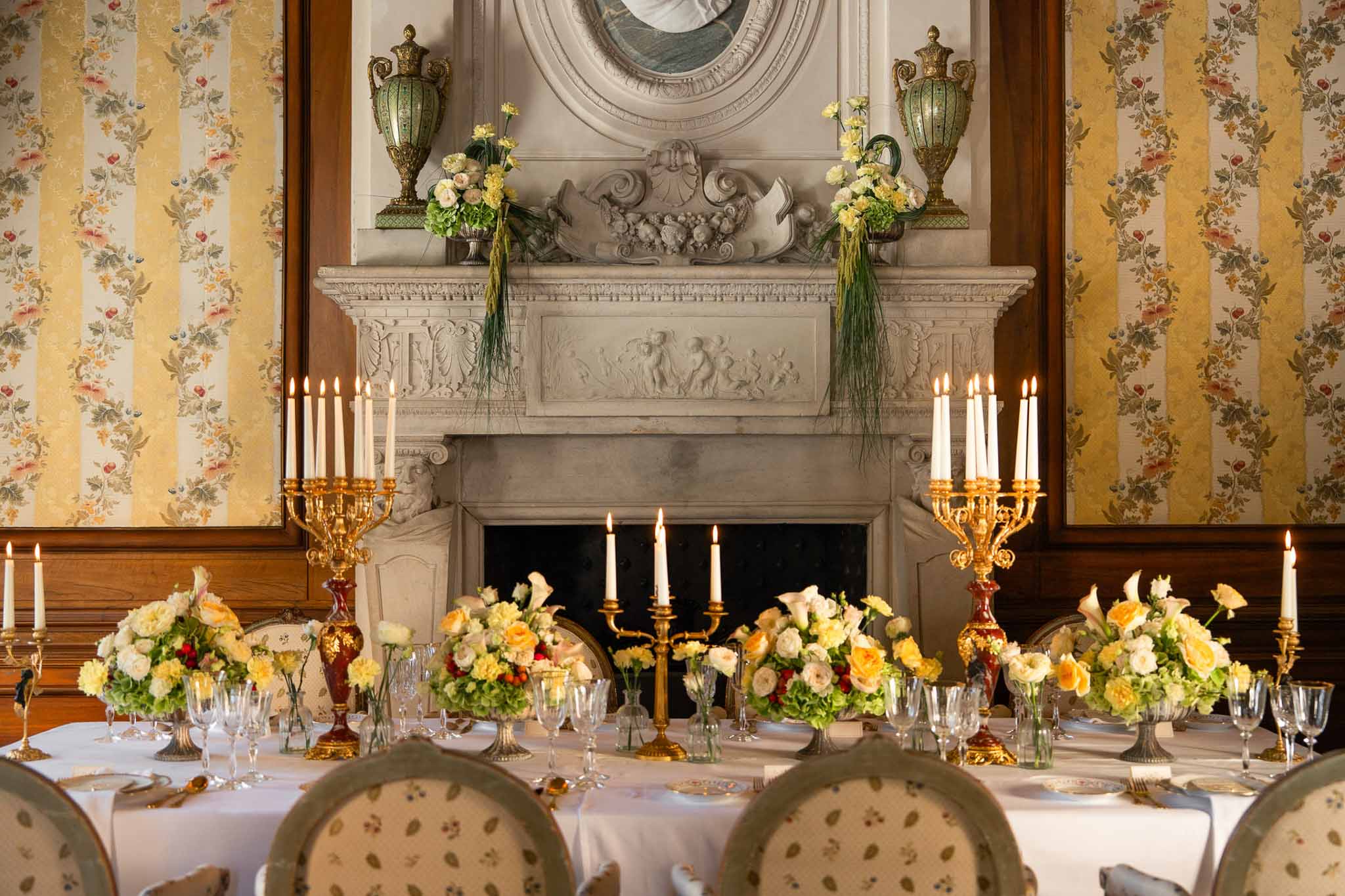 Chateau dining room reception with gold candelabras sage Louis XVI chairs yellow roses and carved marble fireplace