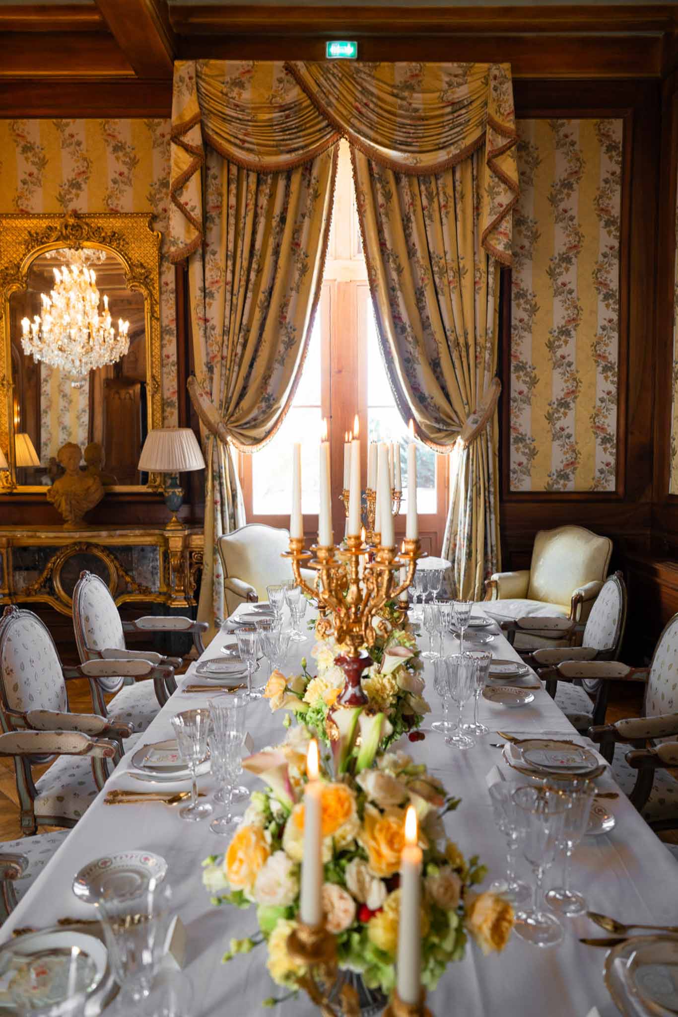 Chateau dining room with gold candelabra peach rose centerpieces Louis XVI chairs crystal chandelier and striped wallpaper