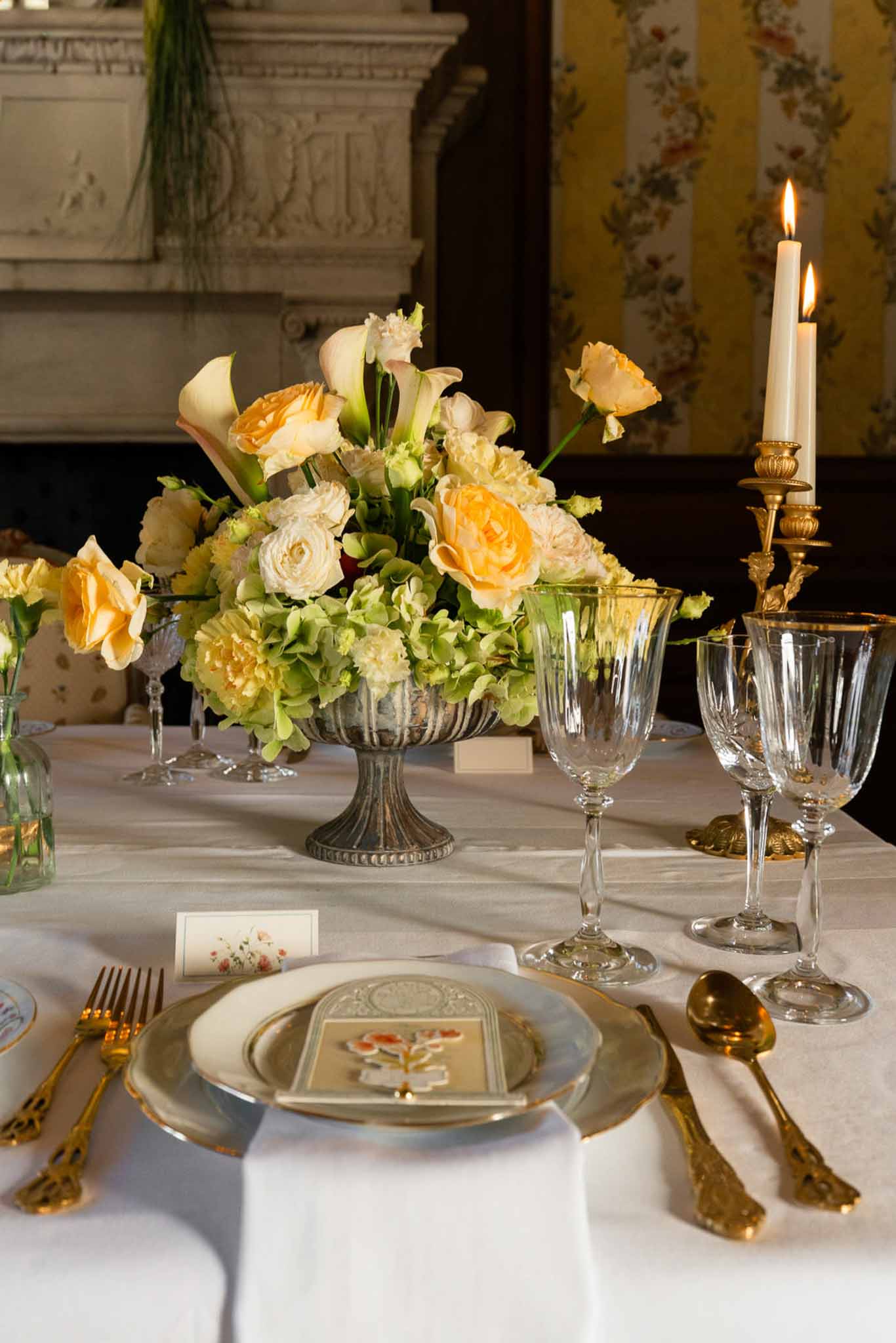 Reception centerpiece of peach roses and calla lilies in silver compote with gold flatware