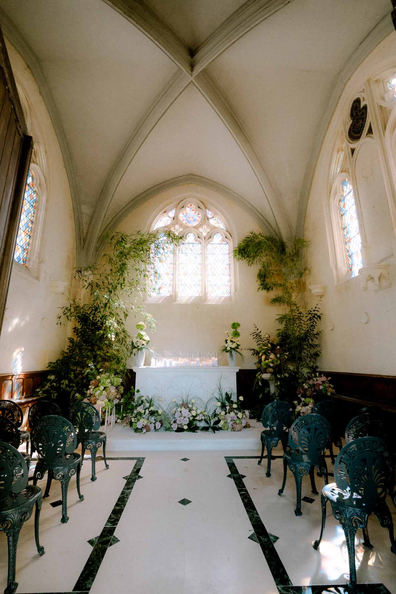 Gothic chapel altar with white rose arrangements, trailing ferns, and blush floral carpet on marble floor