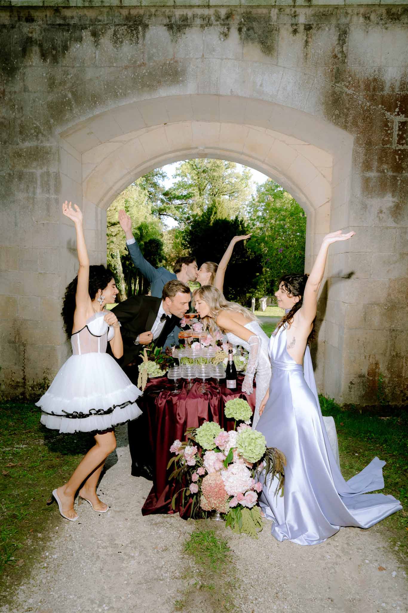 Couple and guests celebrating around a champagne coupe tower beneath a stone chateau archway