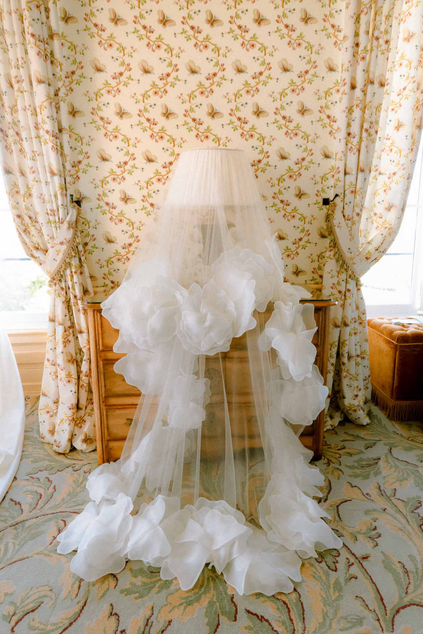 Cathedral veil with organza flower appliques draped over lamp in vintage butterfly-wallpaper room