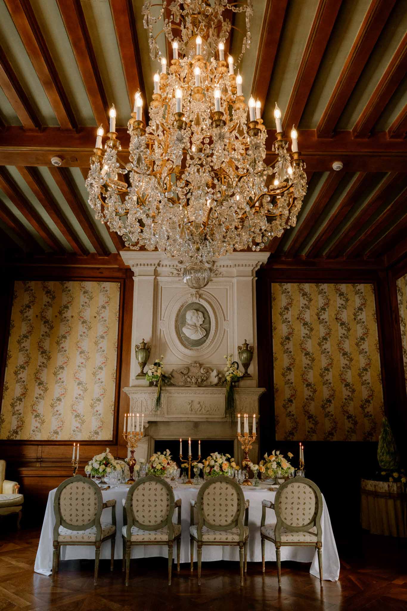 Formal reception table in a chateau dining room with gold candelabras, sage chairs, and stone fireplace
