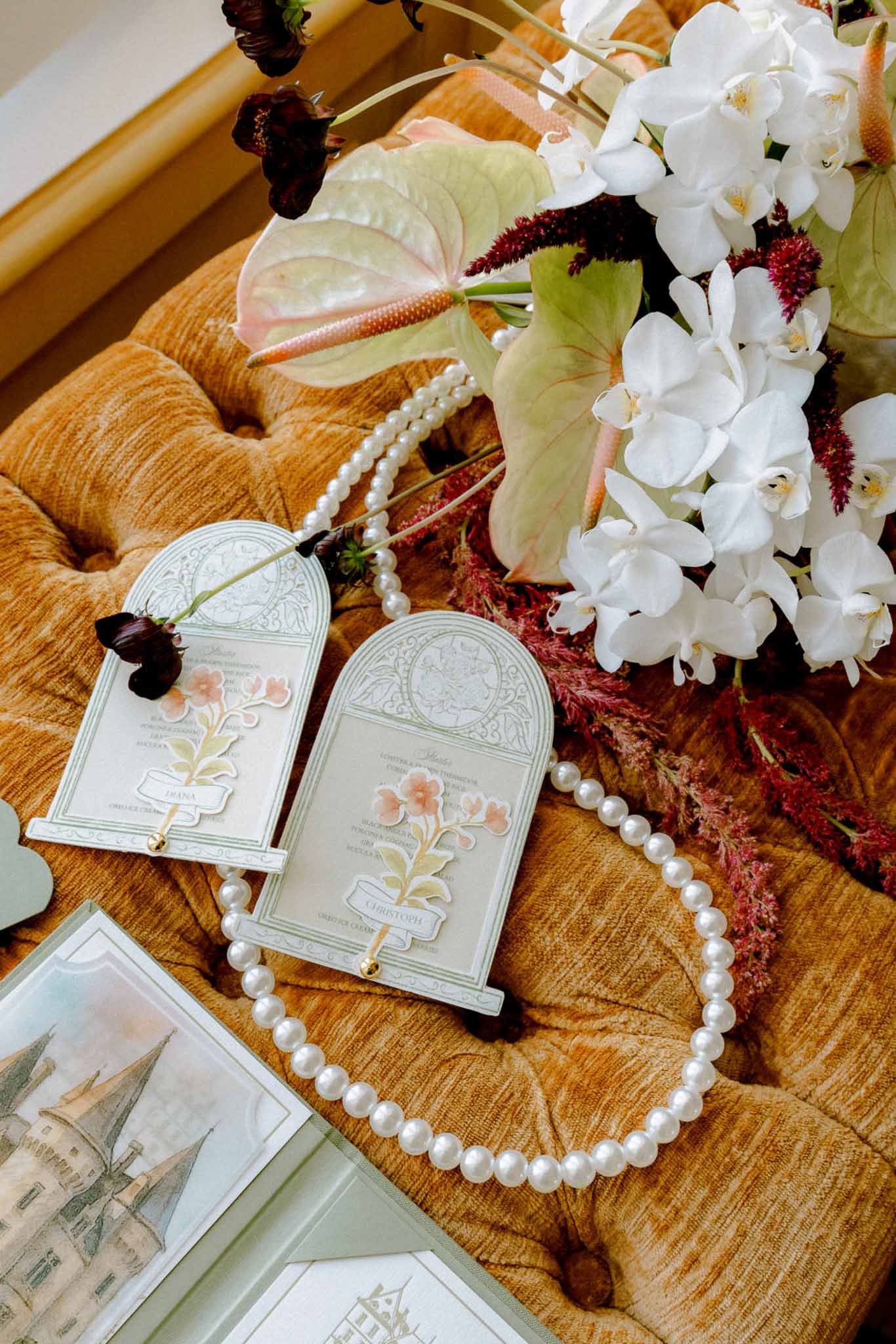 Arch-shaped menu cards with sage borders, pearl necklace, and orchid-amaranth bouquet on burnt orange velvet