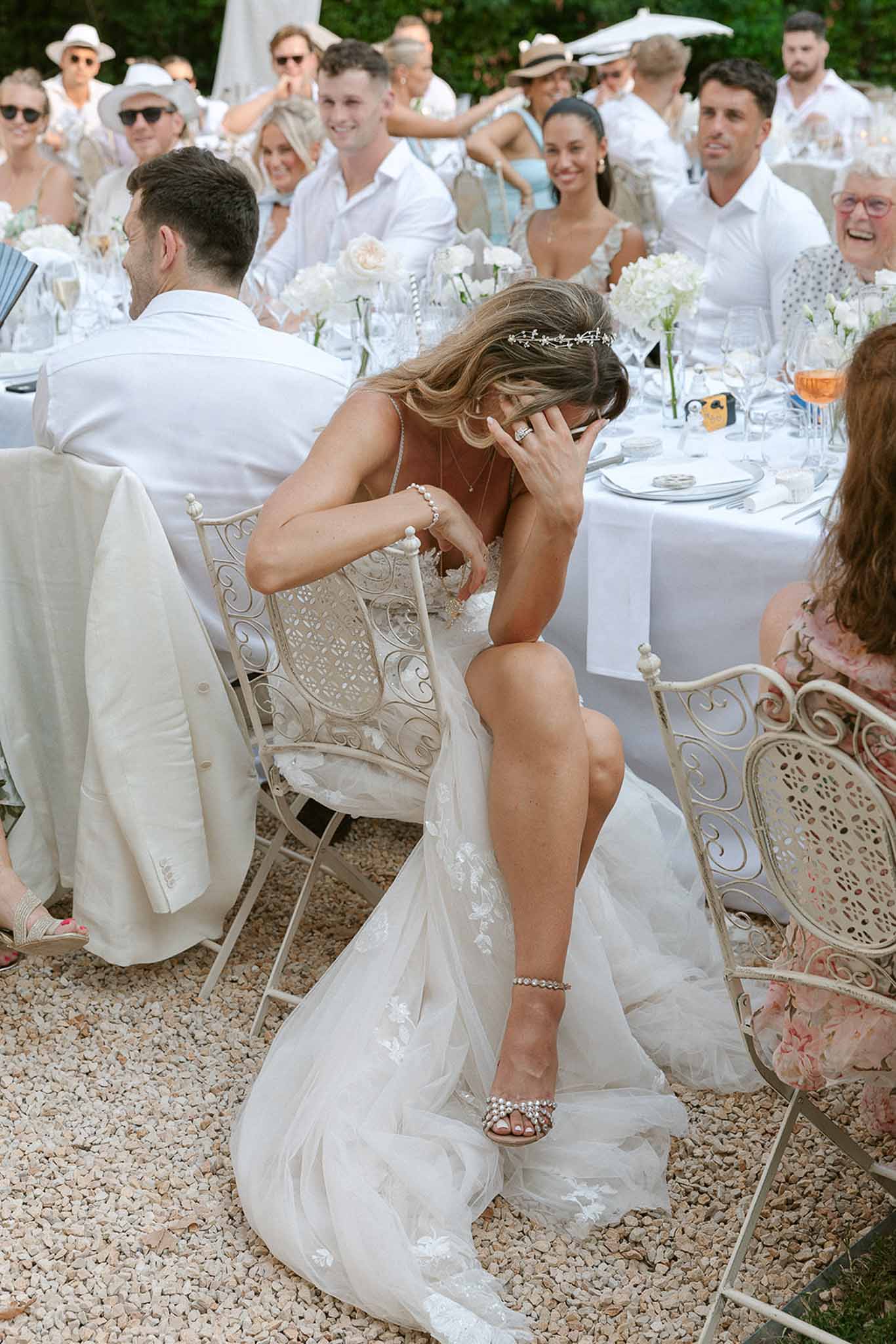 Bride laughing emotionally at head table during outdoor reception speeches with white floral centerpieces