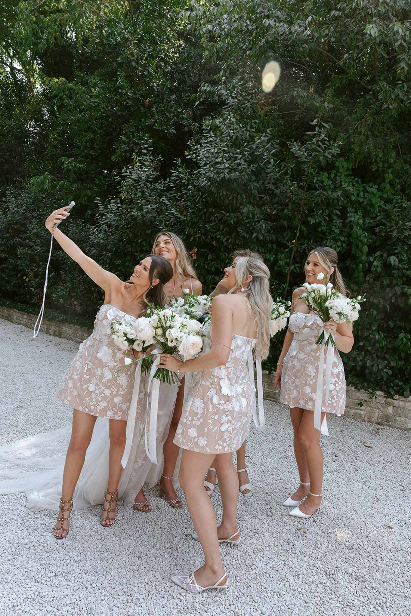 Bride and three bridesmaids in floral mini dresses laughing with bouquets and popping champagne