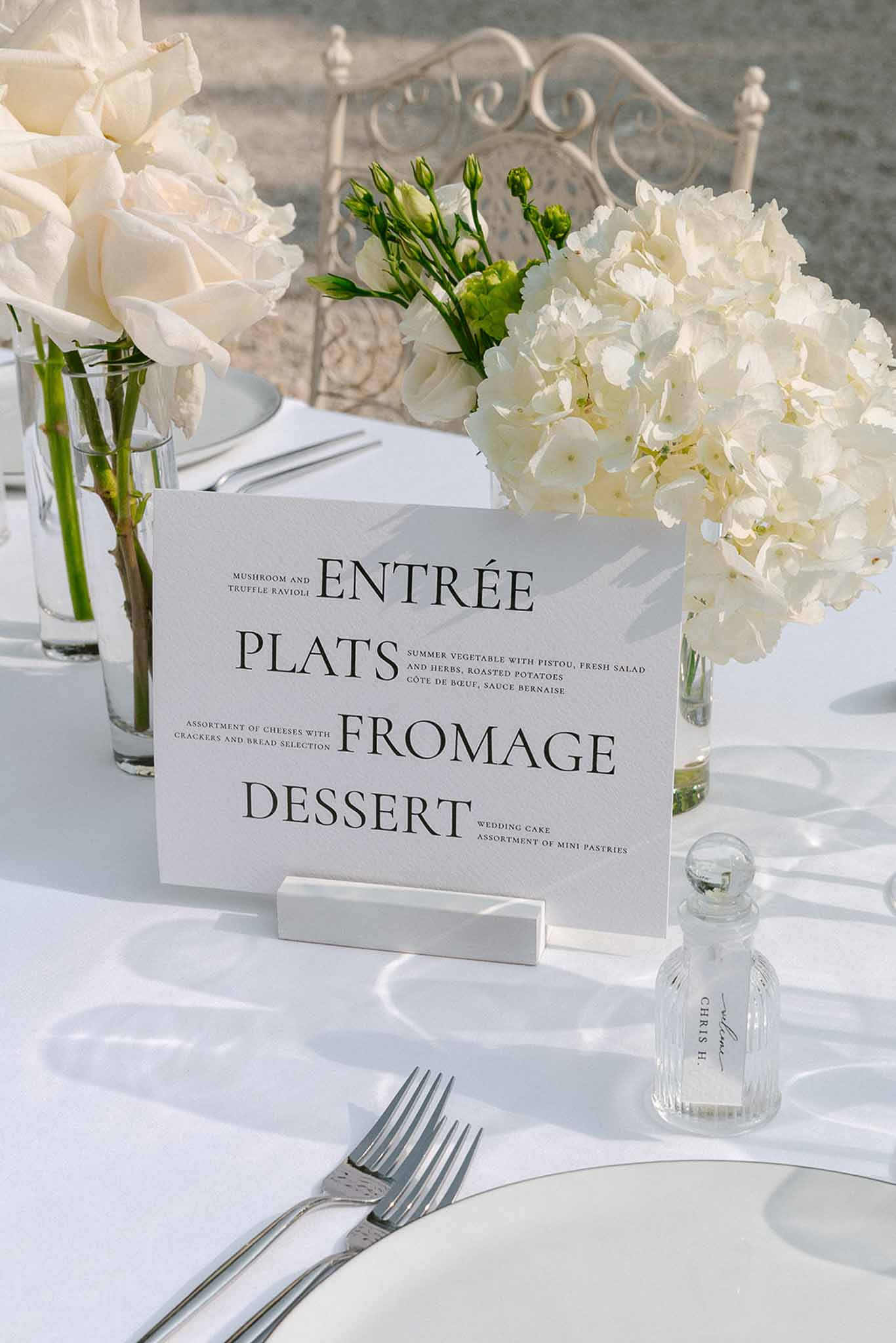 Printed French-English menu card in marble holder on white-dressed reception table with ivory hydrangea arrangements