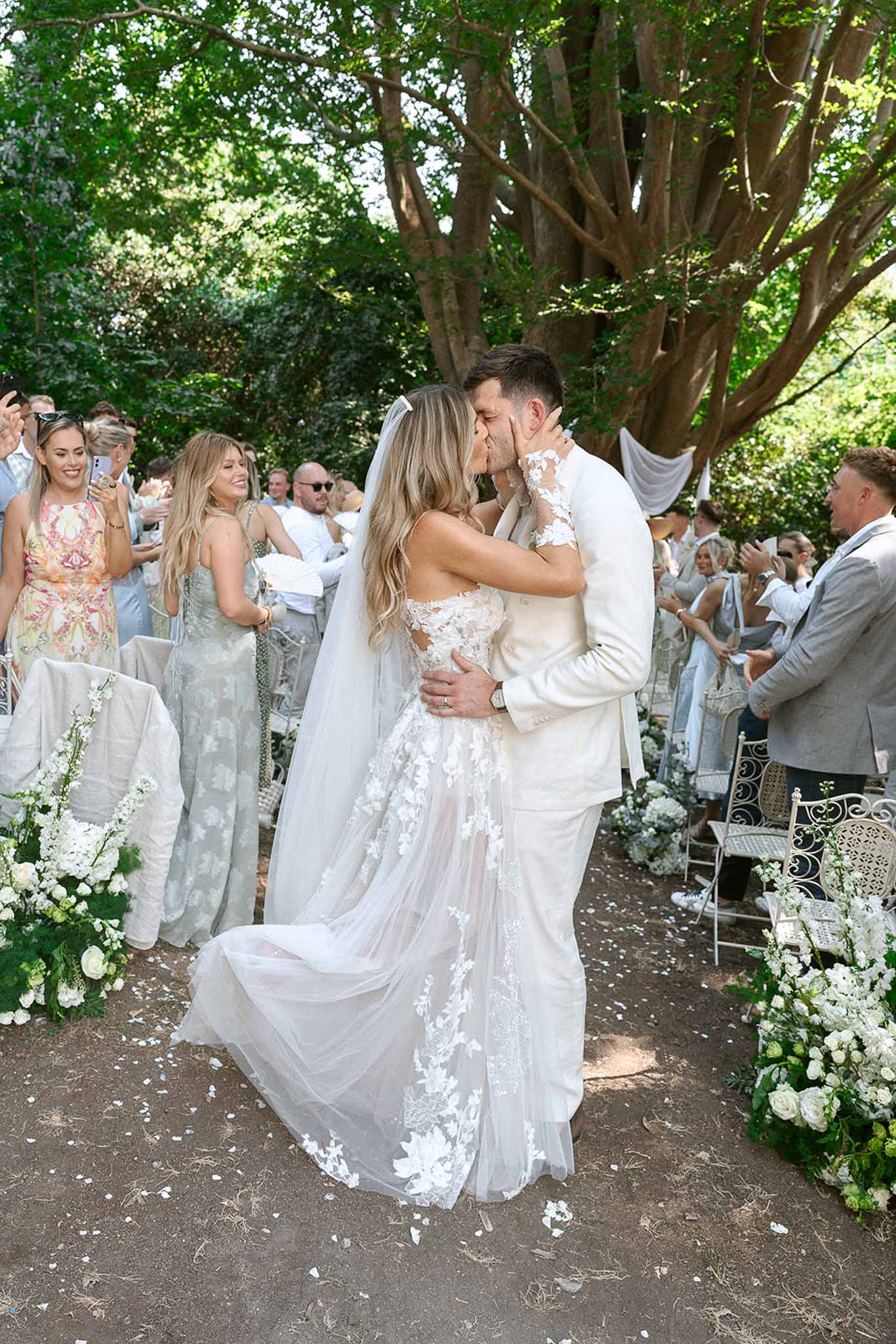First kiss under white rose aisle arrangements as 30 guests applaud in garden ceremony
