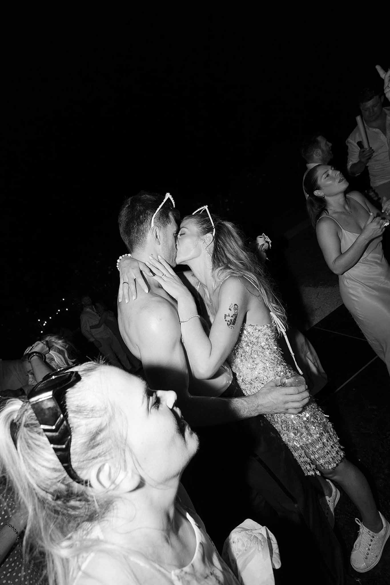 Couple kisses on dance floor at late-night party with sequined mini dress and shirtless groom in B&W