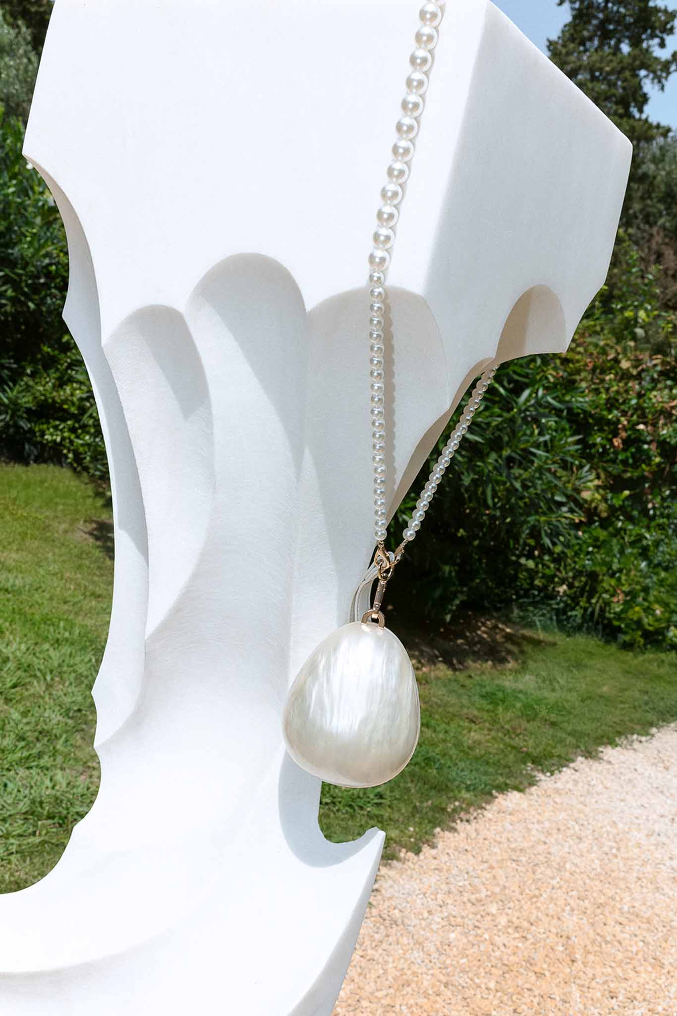 Baroque pearl pendant necklace draped over white sculptural piece in garden setting