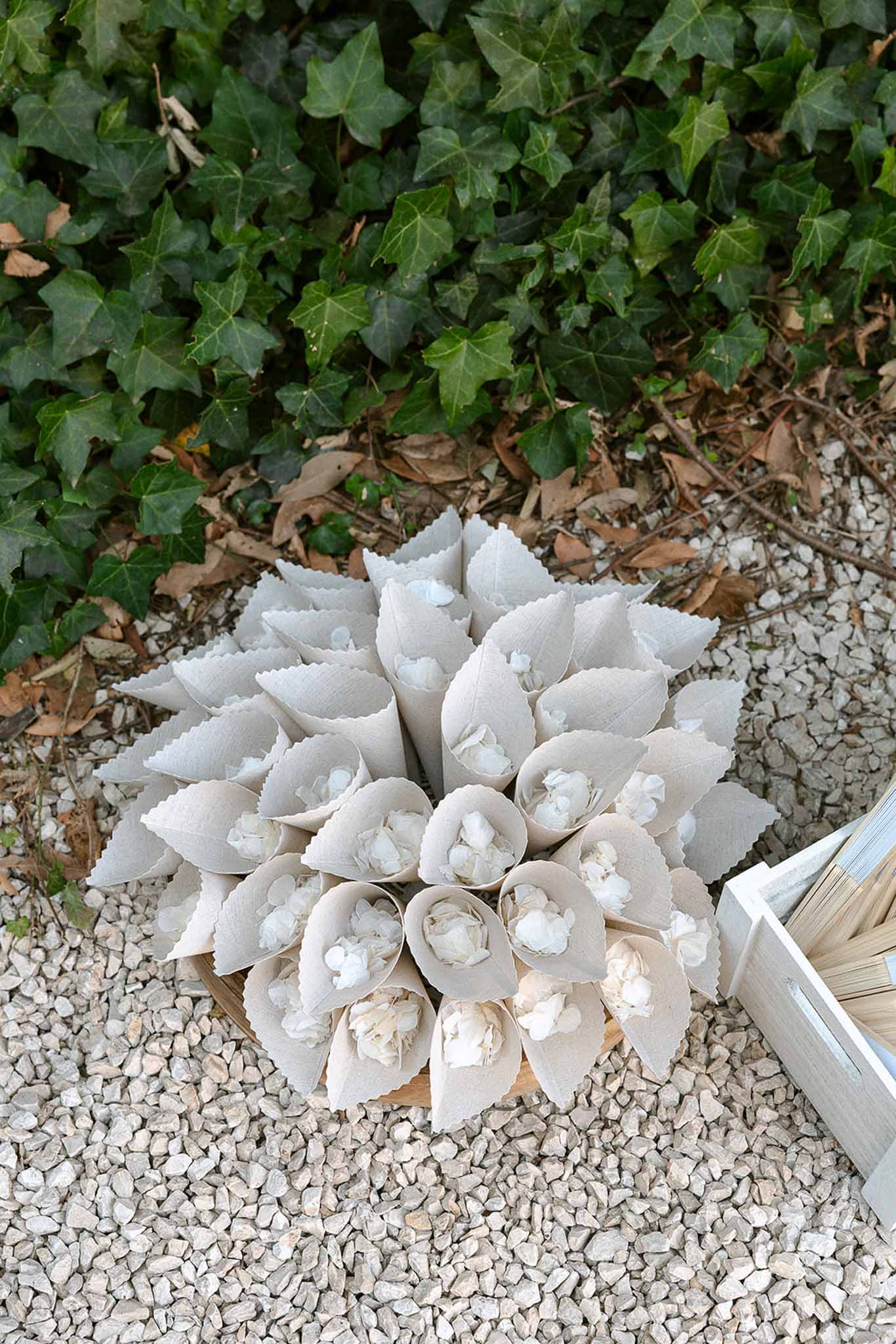 Fan of kraft paper confetti cones filled with white dried petals on wooden board on gravel path