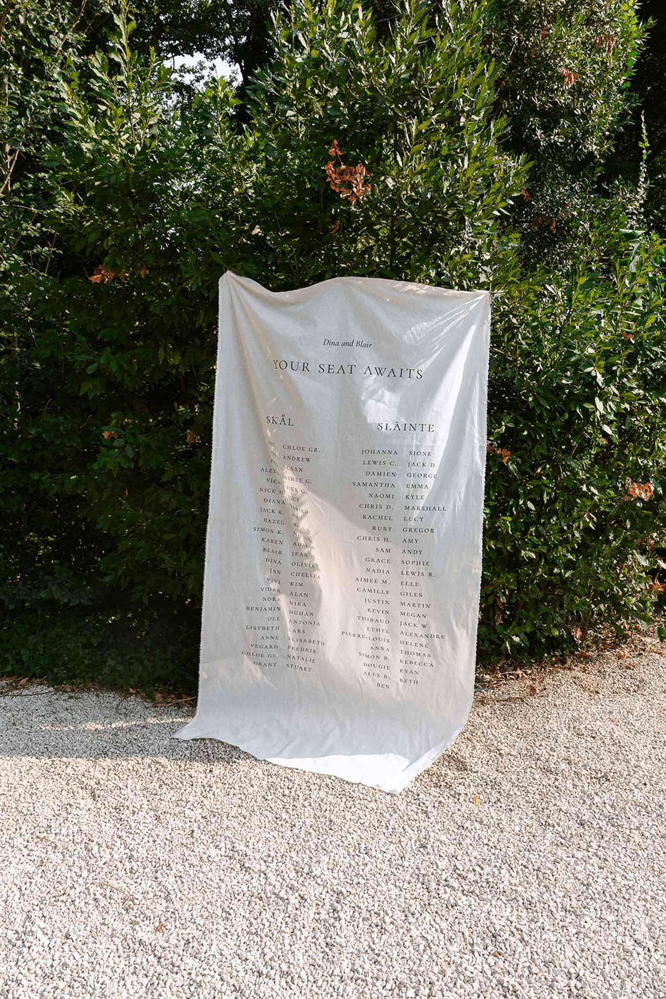Linen seating chart panel reading Your Seat Awaits with Scandinavian and Irish table names on hedge