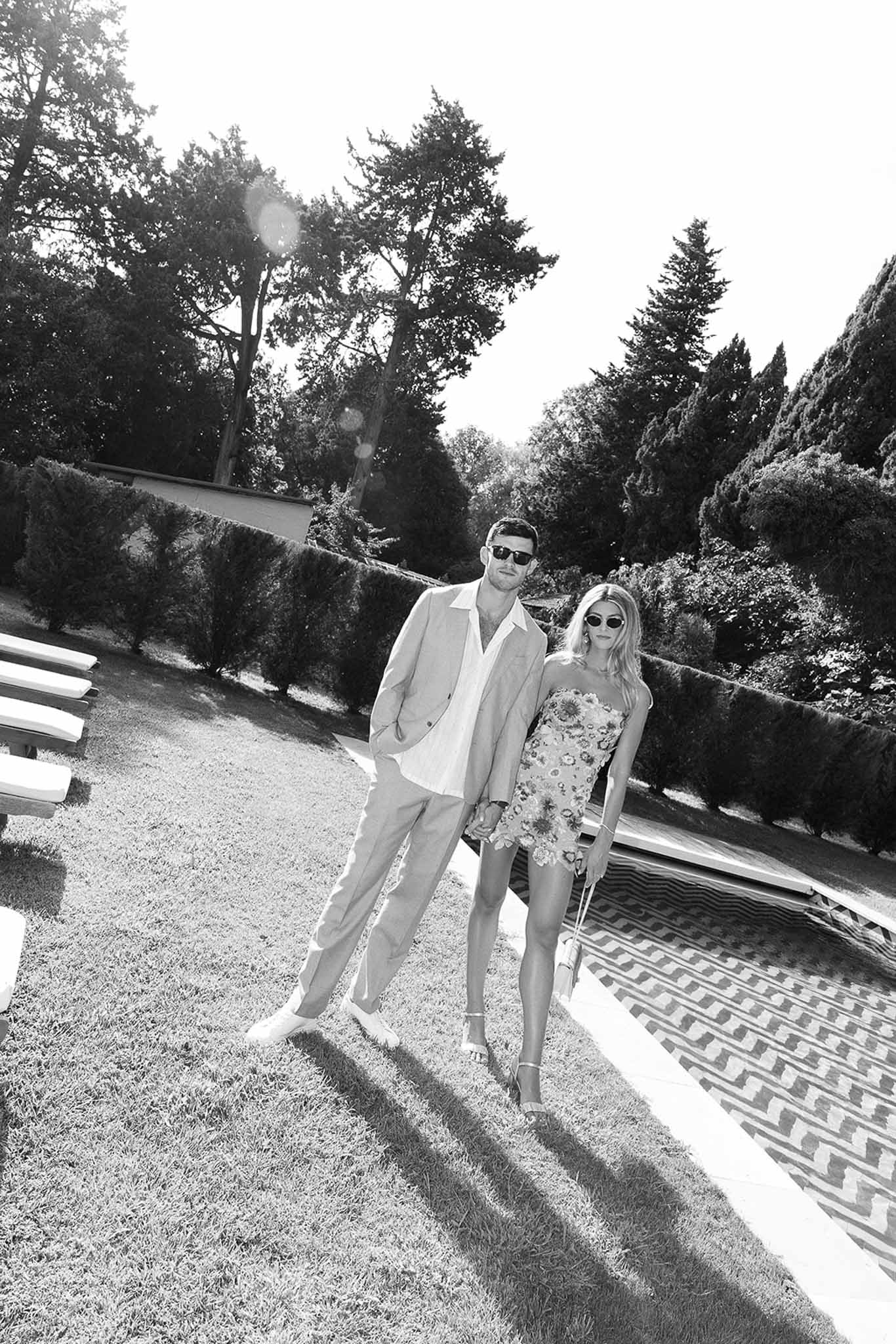 Black and white photo of two wedding guests posing by a pool with chevron tiles at a chateau garden