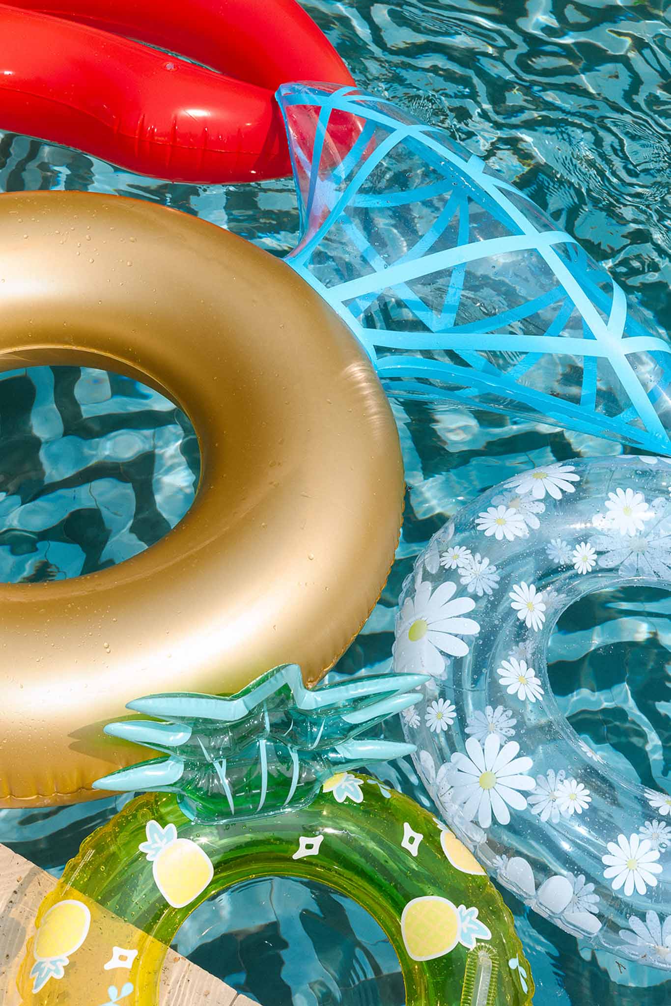 Five colourful inflatable pool floats including diamond ring and pineapple shapes in clear blue pool