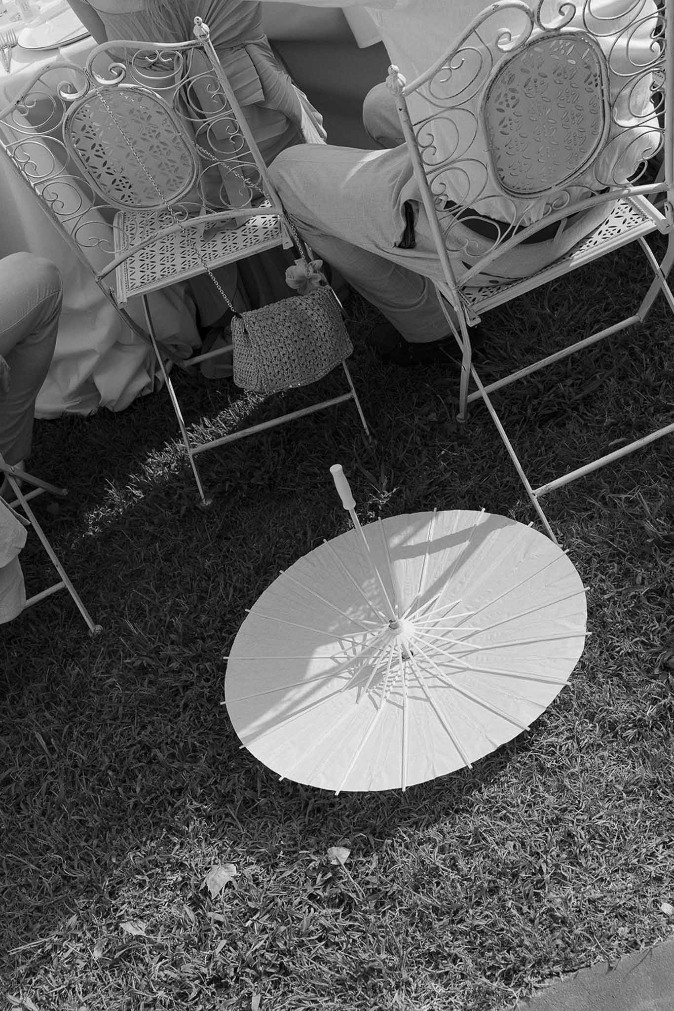 White paper parasol on lawn beside ornate wrought-iron garden chairs at outdoor reception in B&W
