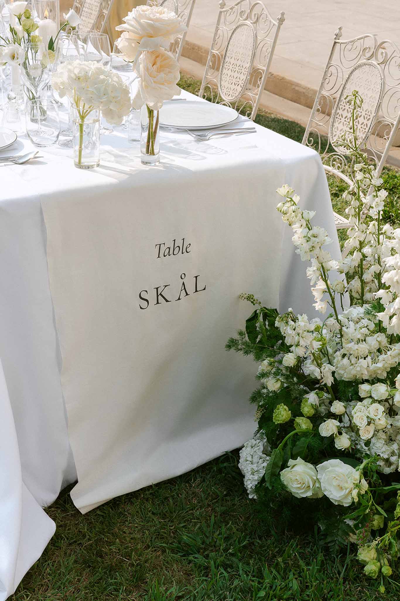 All-white reception table with printed linen table name garden rose bud vases and ground floral cascade