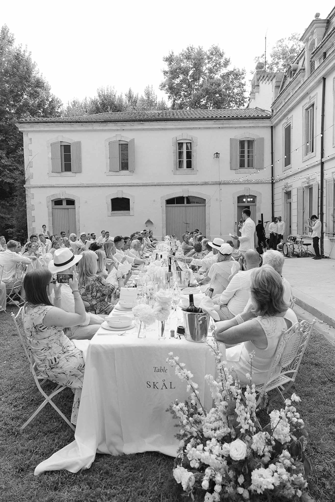 Black and white 50-guest dinner at long table with white dress code, live band, and fairy-lit courtyard