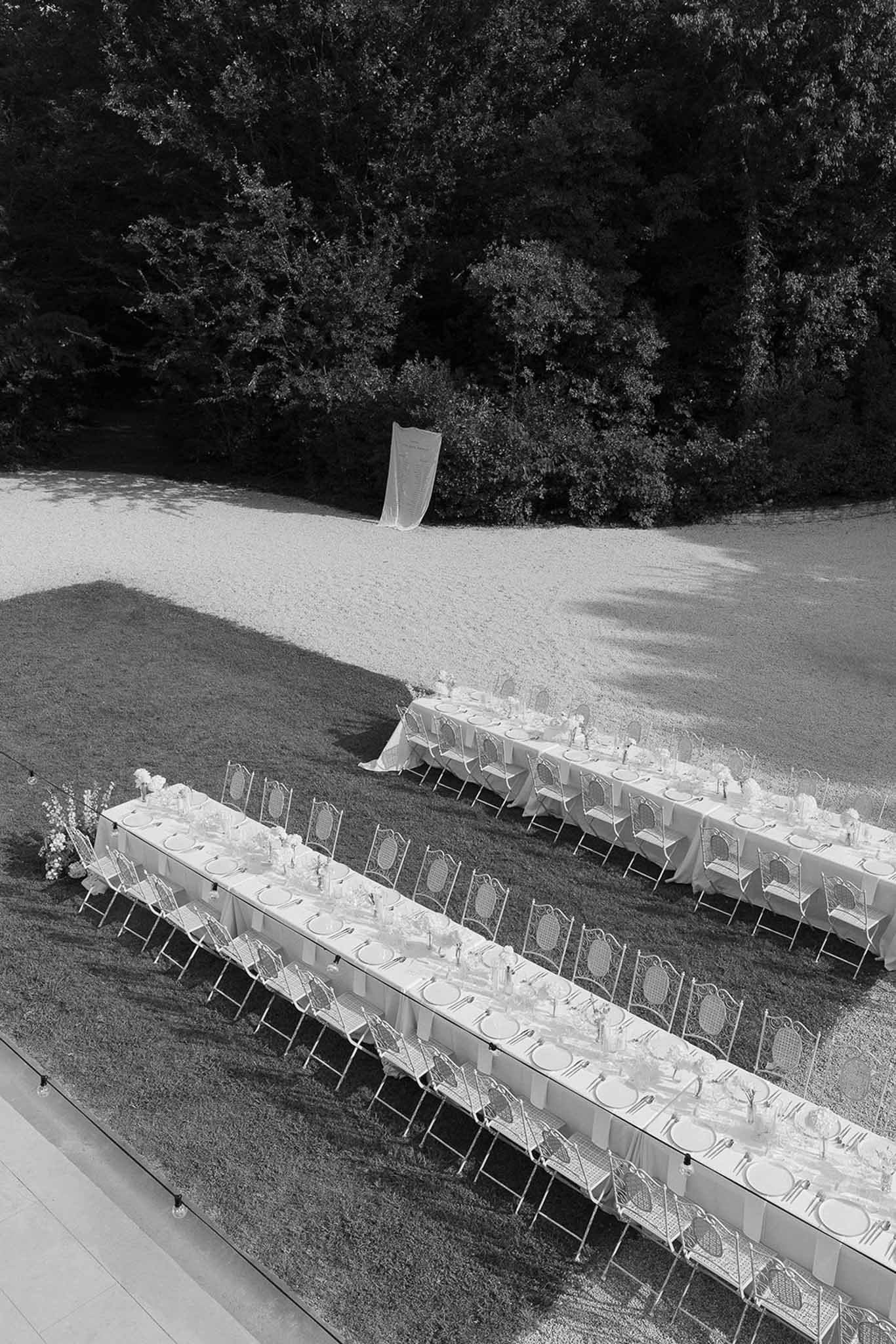 Black and white aerial view of two long reception tables with white chairs on lawn