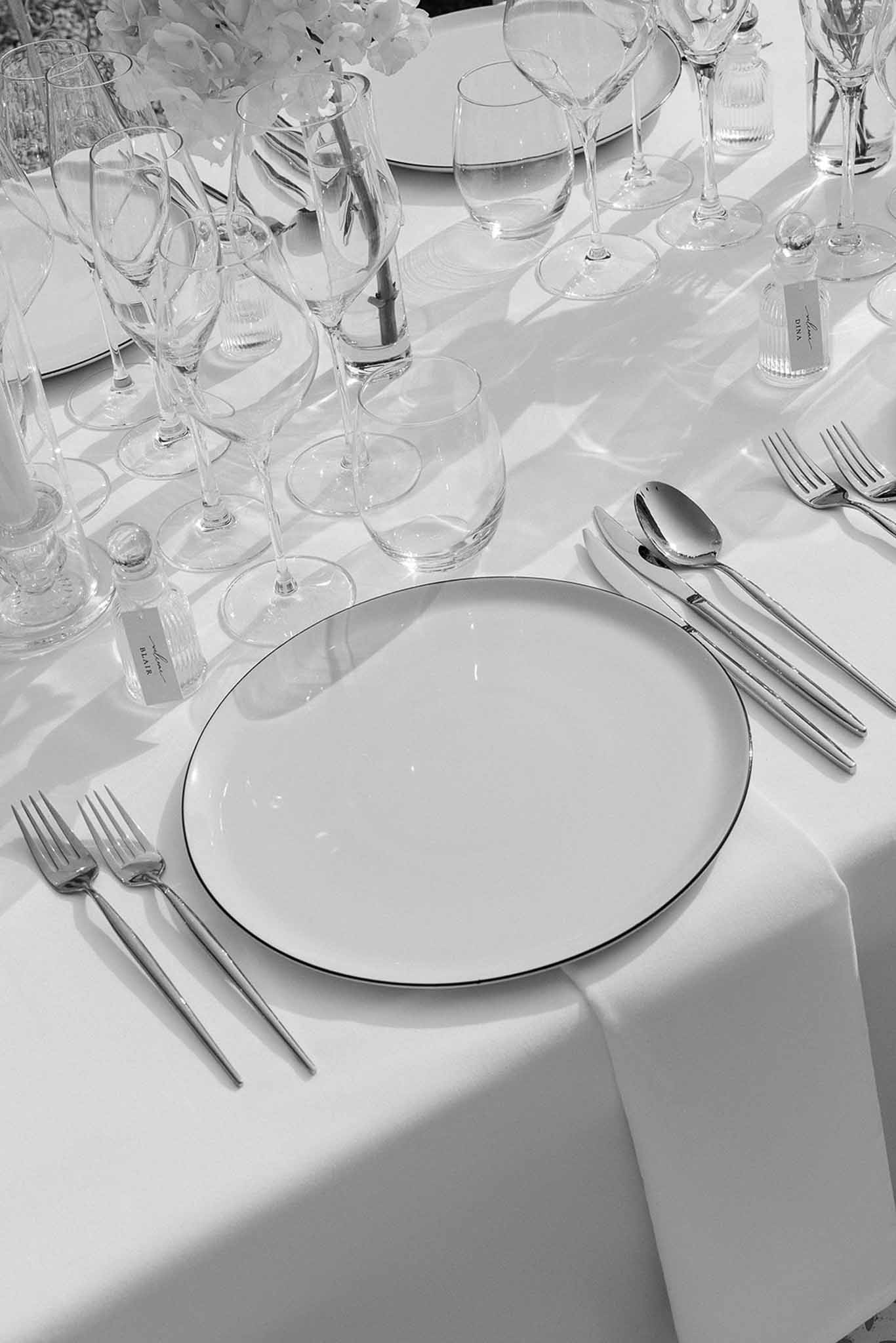 Black-and-white close-up of formal place setting with silver cutlery, crystal glasses, and white floral arrangements