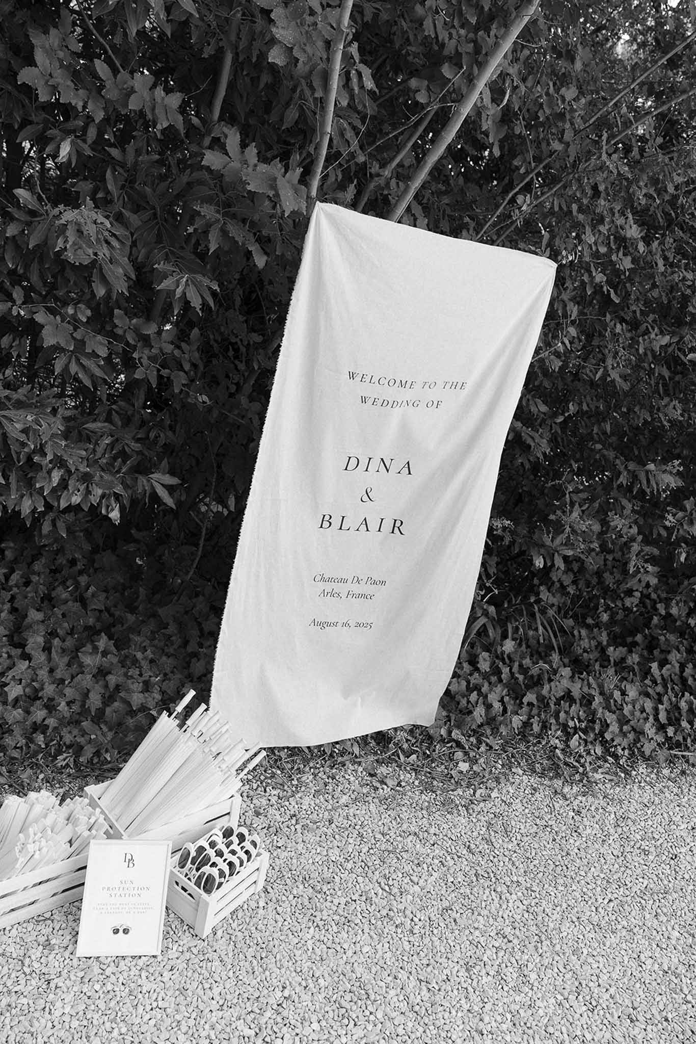 Black and white welcome banner reading Dina and Blair with sun protection station of parasols and sunglasses