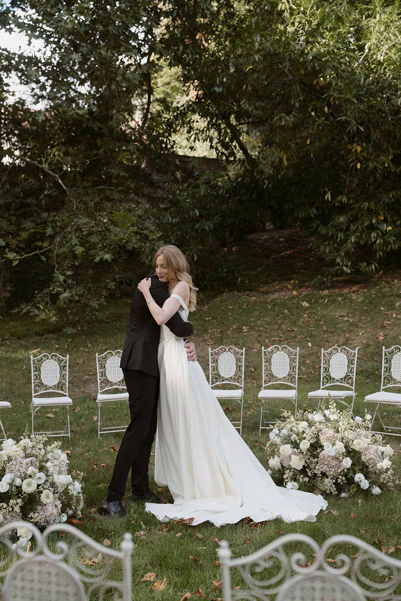 Couple embracing at ceremony altar surrounded by white ranunculus and blush hydrangea ground arrangements