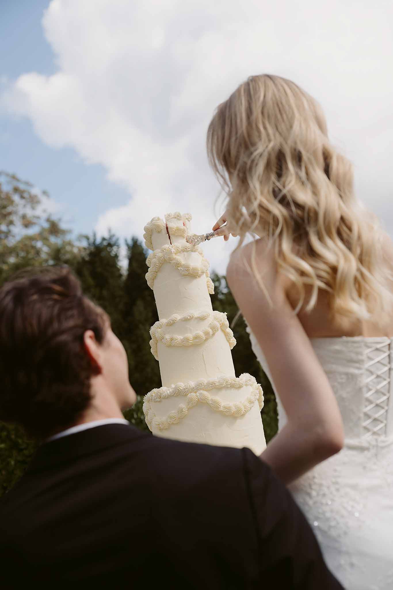 Couple cutting four-tiered ivory buttercream rosette cake with silver knife at reception