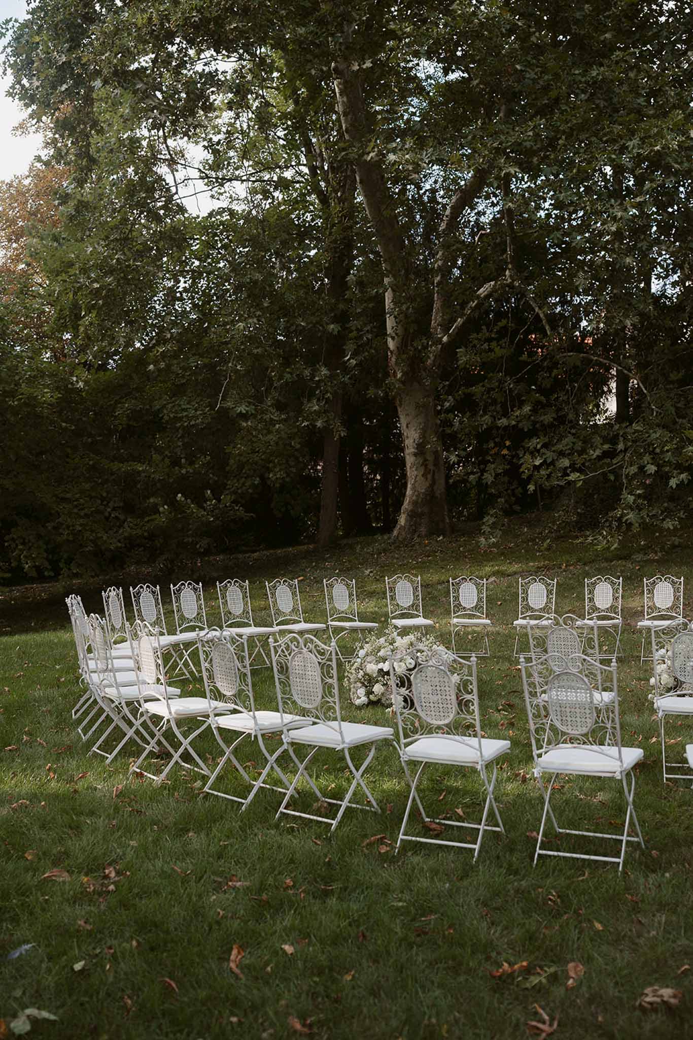 White wrought-iron folding chairs arranged in curved rows on a lawn for an outdoor wedding ceremony before guests arrive