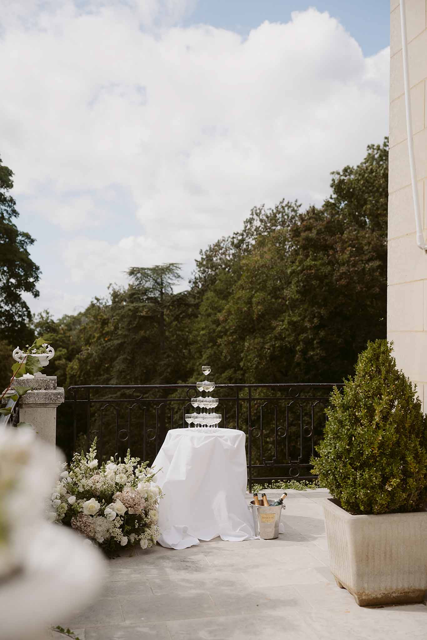 Champagne coupe tower on draped table with floral arrangement on chateau stone terrace