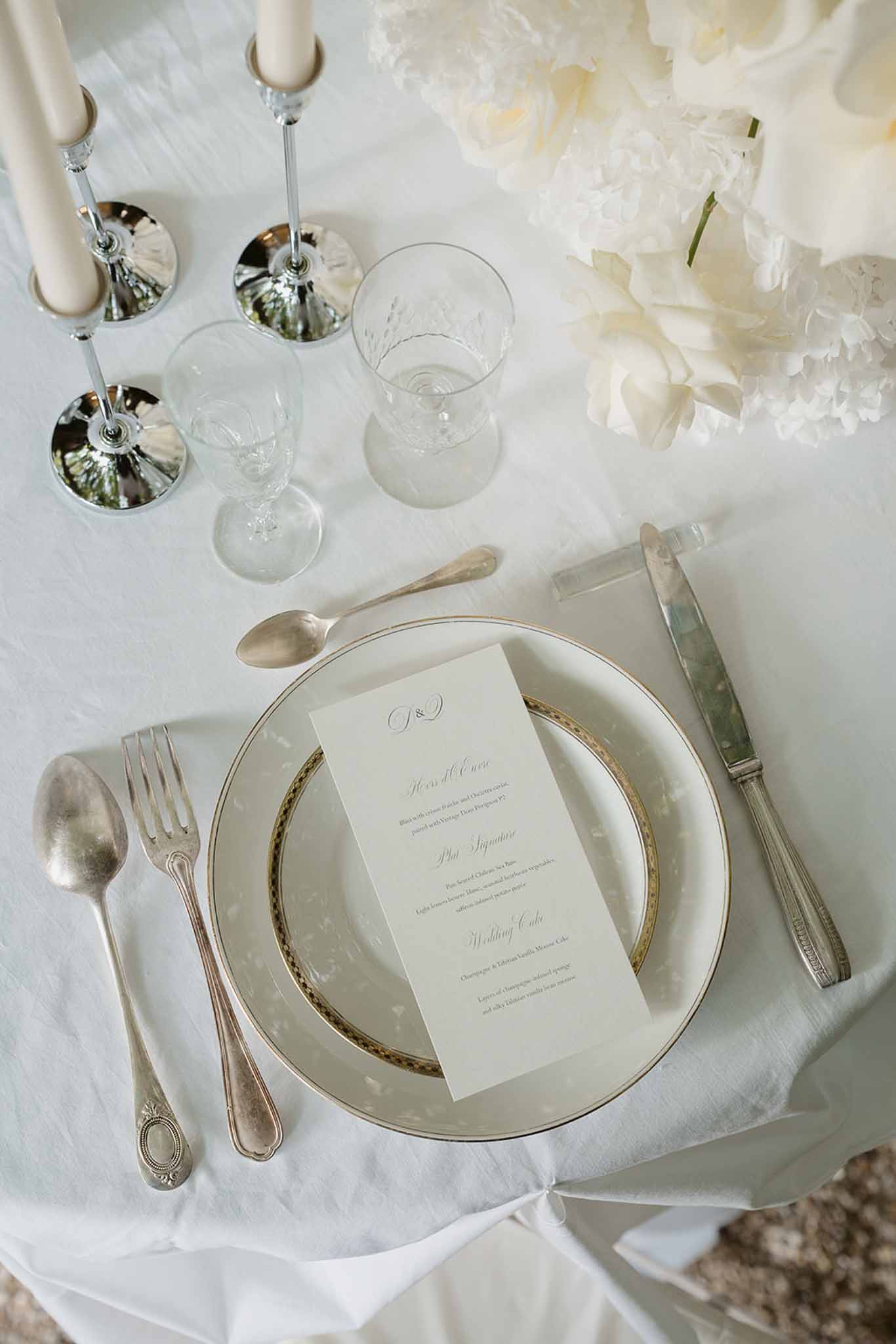 All-white place setting with gold-rimmed china, monogrammed menu, and white peony and hydrangea centerpiece