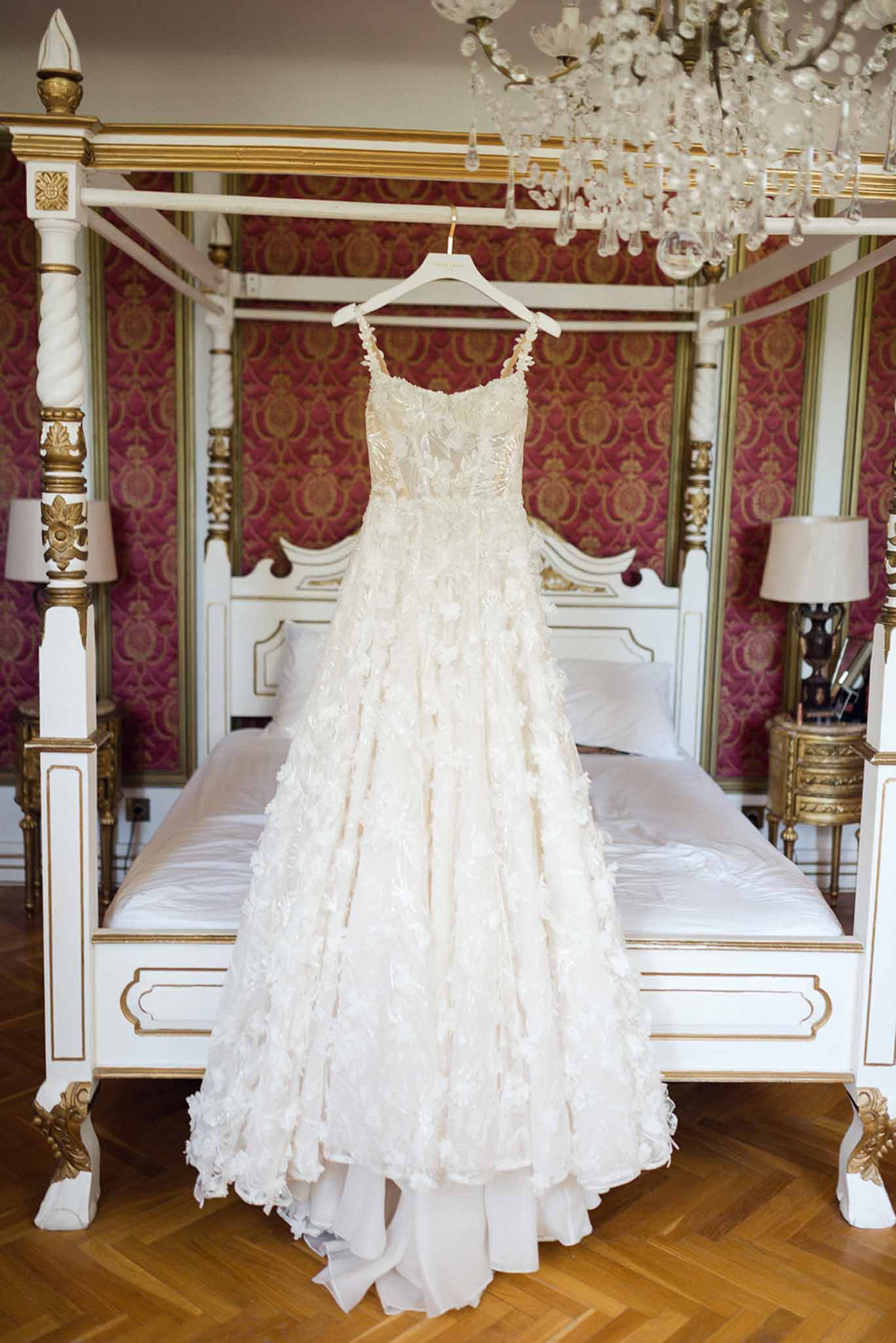 Ivory A-line wedding gown with floral appliques hanging from four-poster bed in ornate room