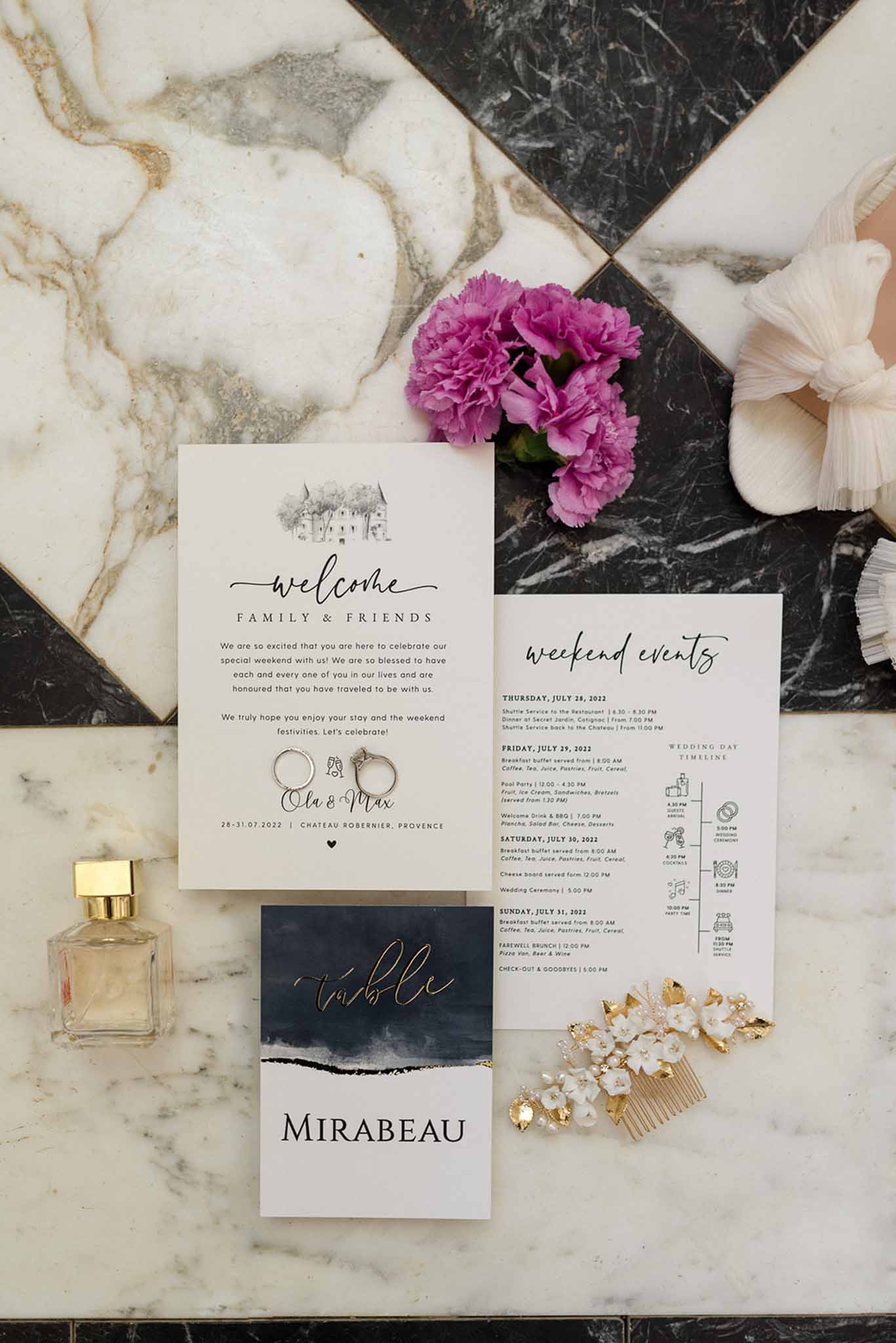 Flat lay of wedding stationery, gold rings, perfume bottle, hair comb, and magenta carnations on marble tiles