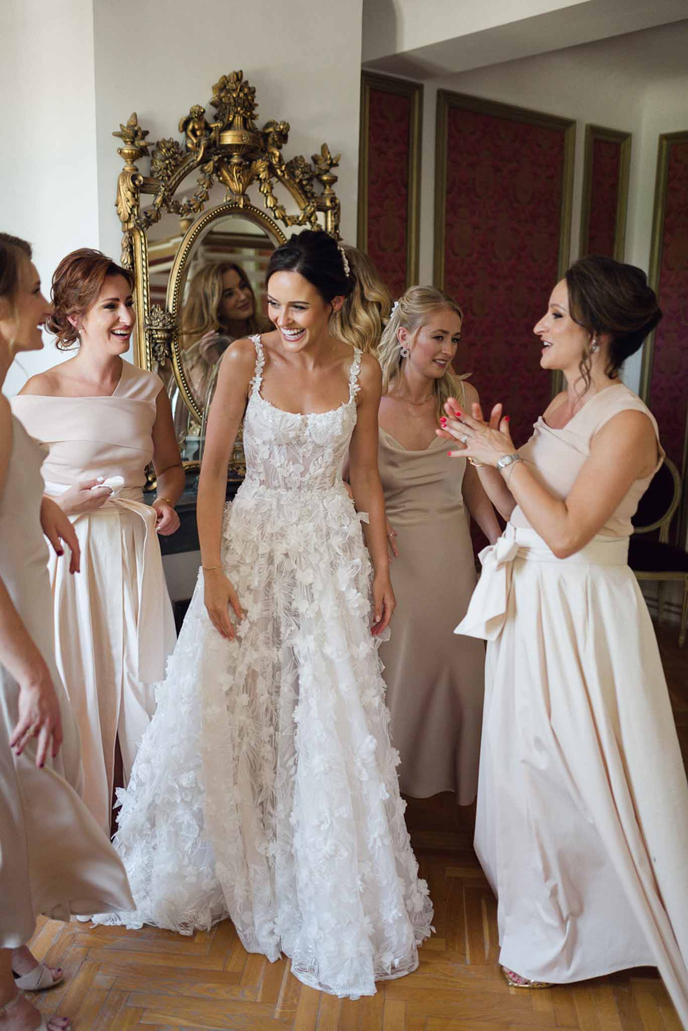 Bride in floral applique gown with four bridesmaids in blush and champagne dresses in crimson-panelled room