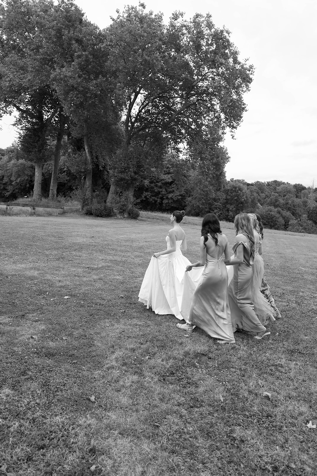 Black and white photo of bride and four bridesmaids walking across a lawn seen from behind