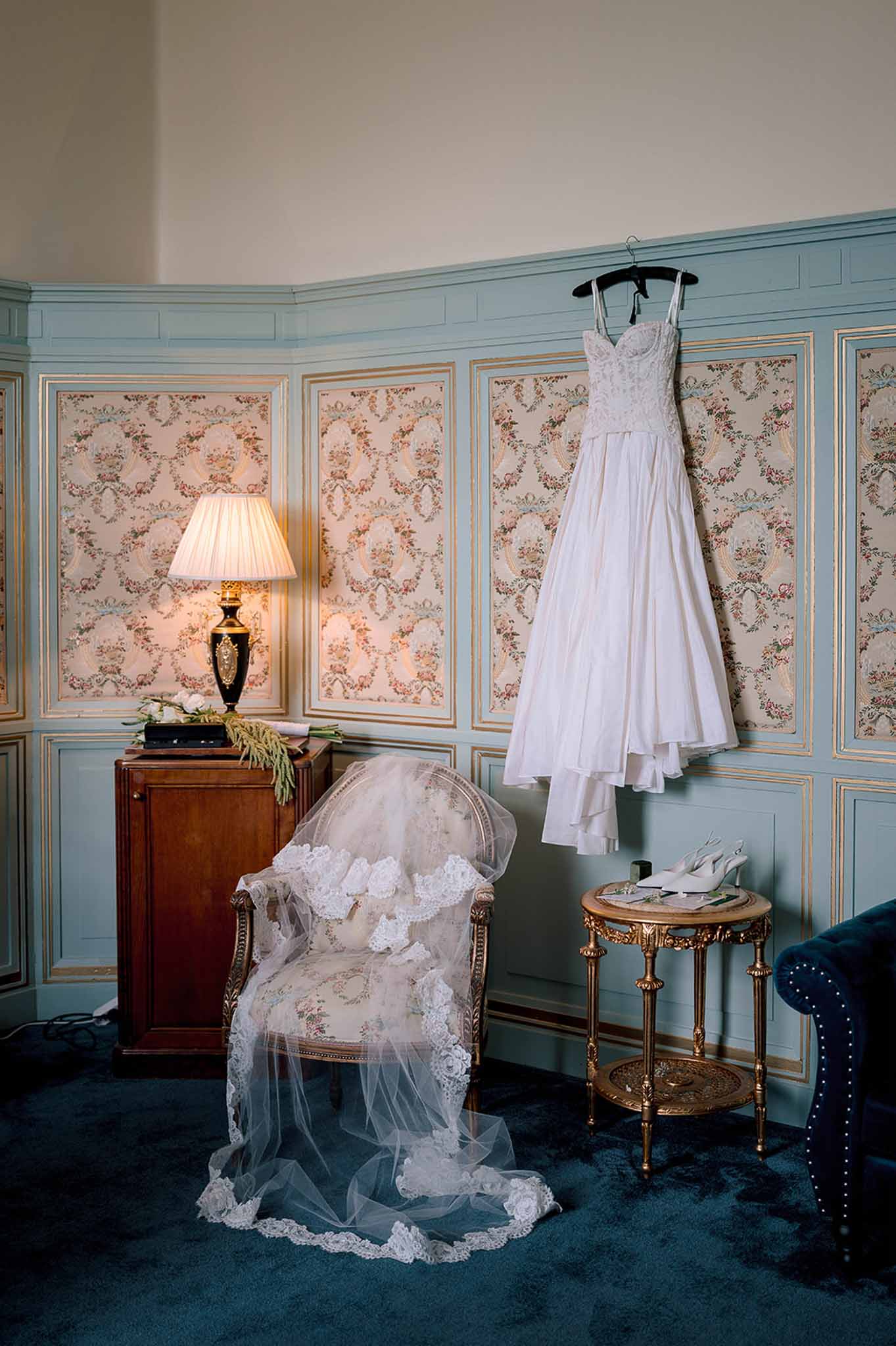 Lace-bodice gown and floral veil in blue-panelled chateau room with gilt boiserie and gold armchair