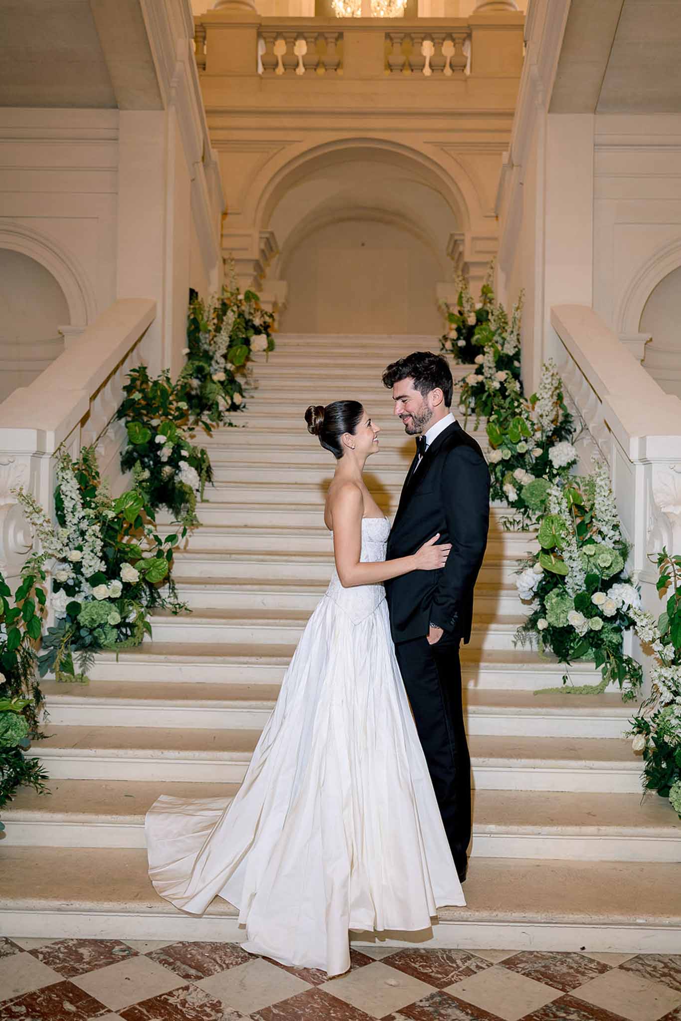Bride and groom on marble staircase lined with white hydrangea and green anthurium in grand foyer