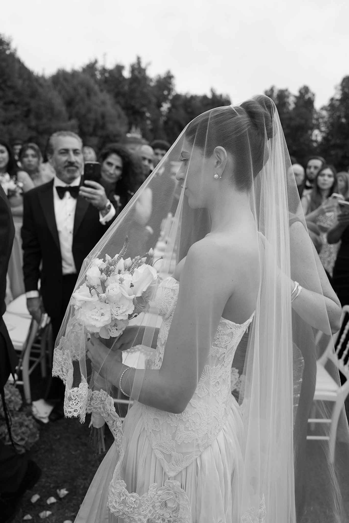 Black and white photo of bride walking down the aisle in strapless lace ballgown with cathedral veil and bouquet