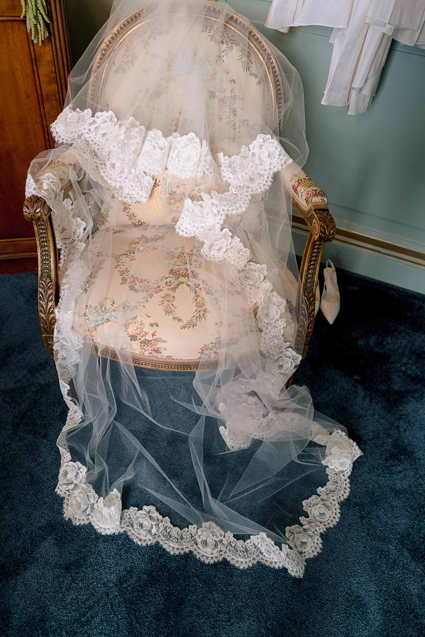 Cathedral-length ivory bridal veil with floral lace trim draped over gold-framed armchair with bridal shoes nearby
