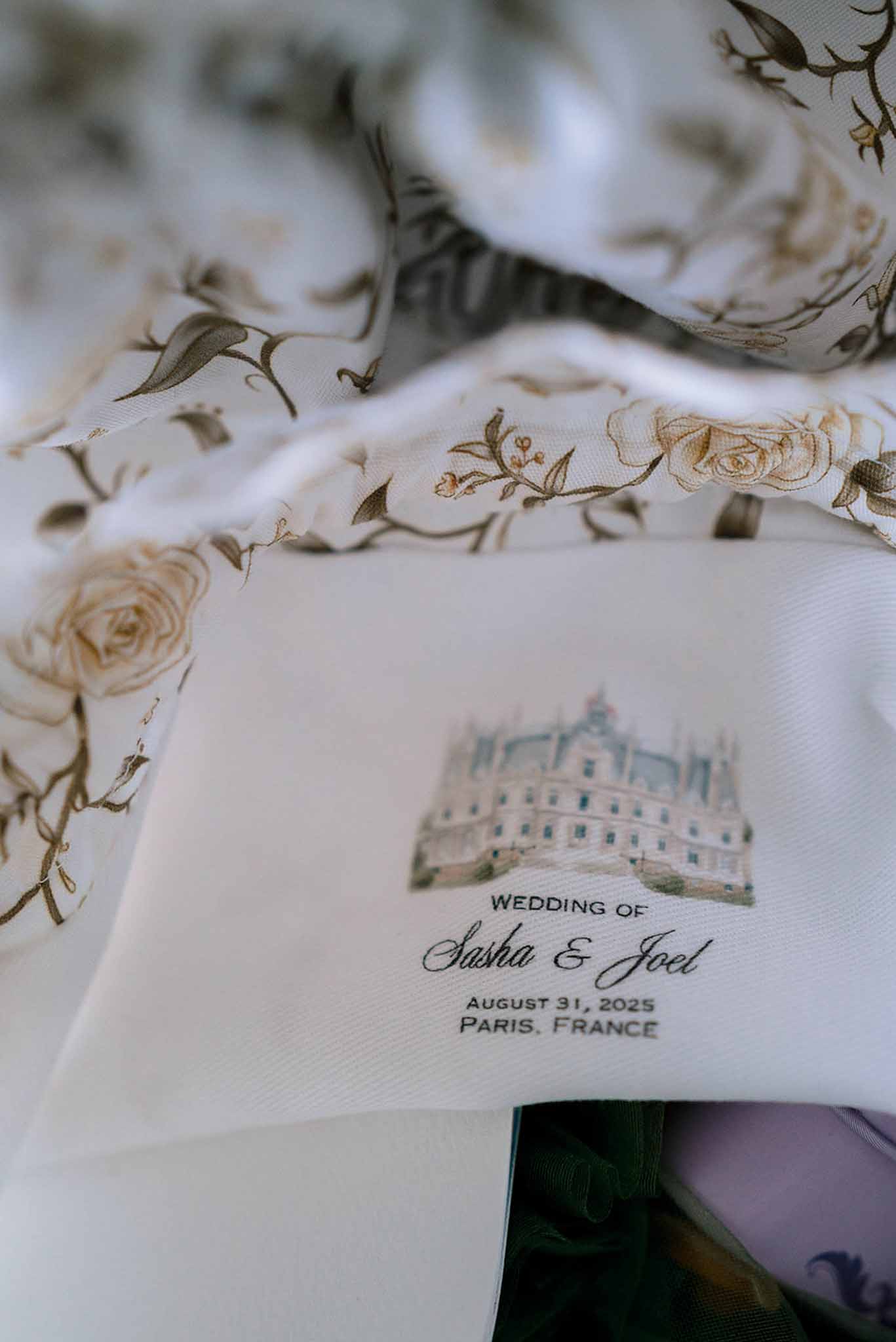 Cream ceremony program with watercolour chateau illustration layered on ivory rose-print fabric