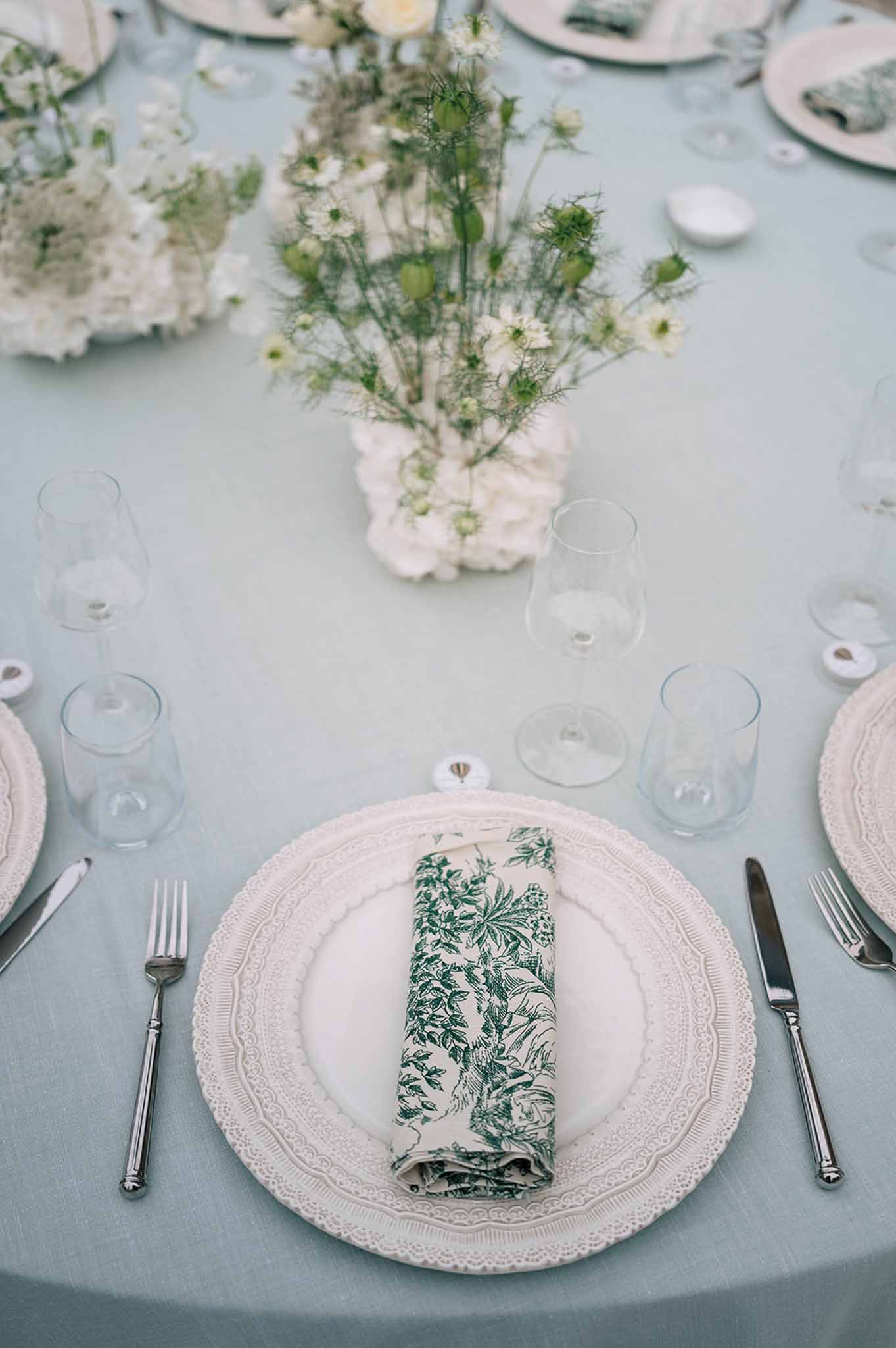 Reception place setting with scalloped charger plate, toile de Jouy napkin, and white floral centerpiece