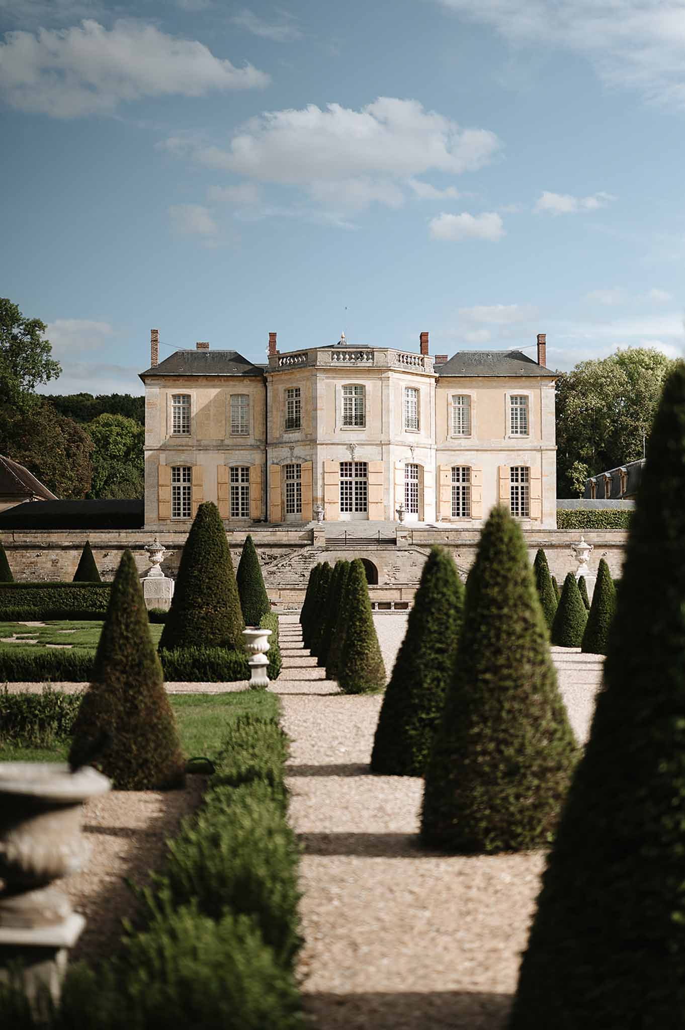 French chateau with golden limestone facade and formal parterre garden with topiary yews and gravel pathways