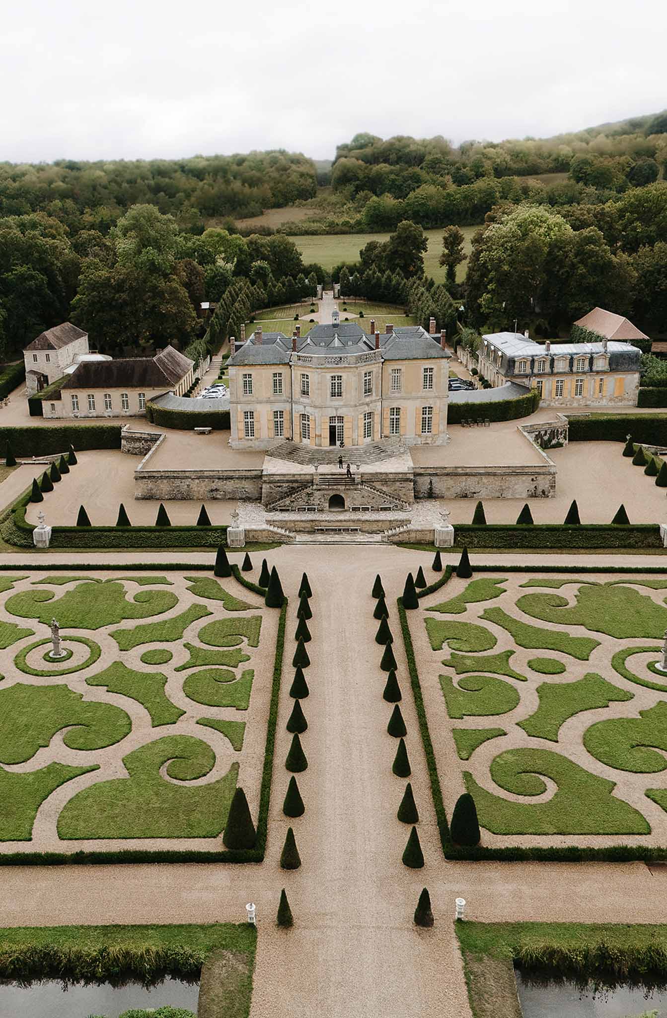 Aerial 18th-century chateau with mansard roof parterre broderie garden conical topiary and central gravel allee