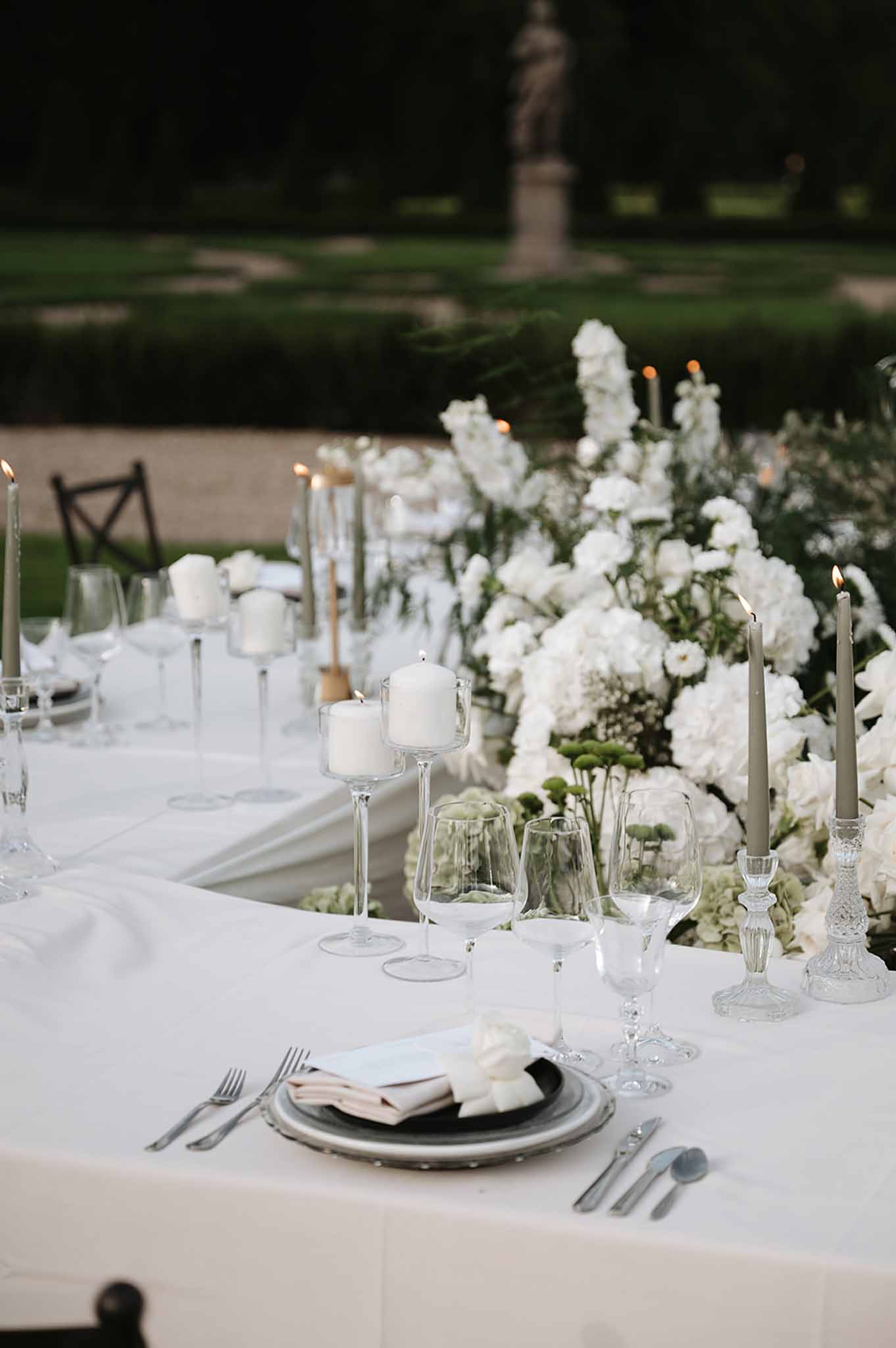 Garden reception table with white hydrangea and ranunculus centerpiece, sage taper candles, and crystal glassware