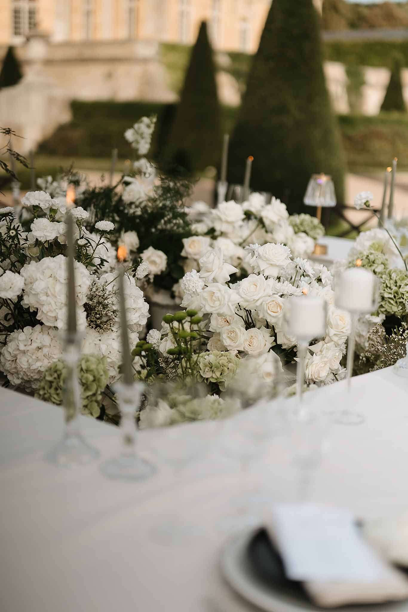 All-white and green floral centerpiece with silver candelabras on reception table before chateau
