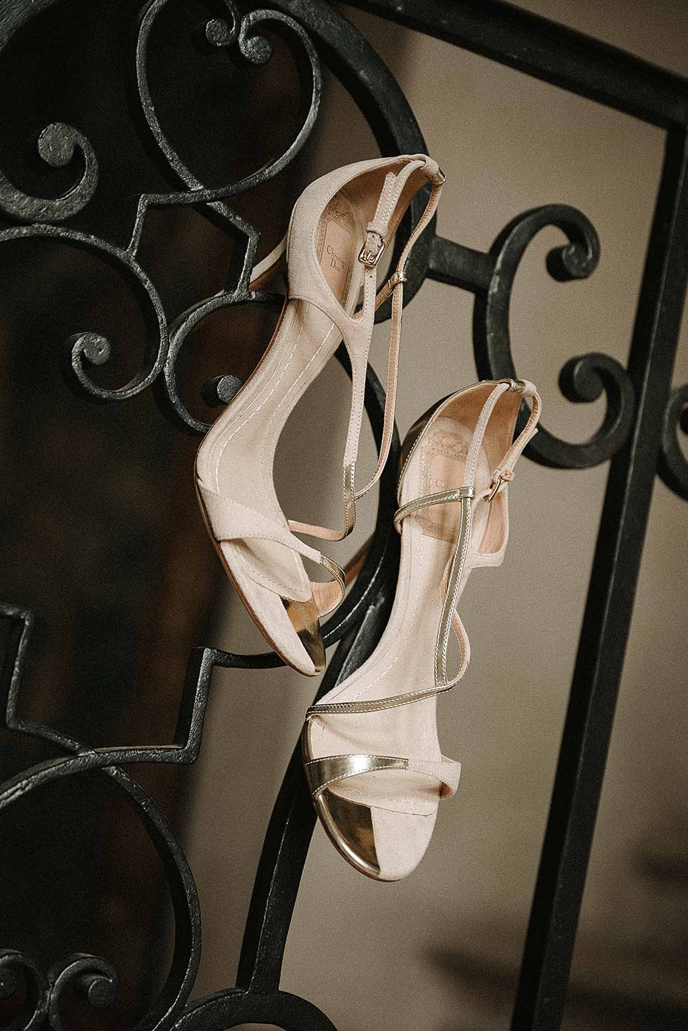 Nude and gold bridal heeled sandals with ankle strap resting on ornate wrought iron scrollwork railing