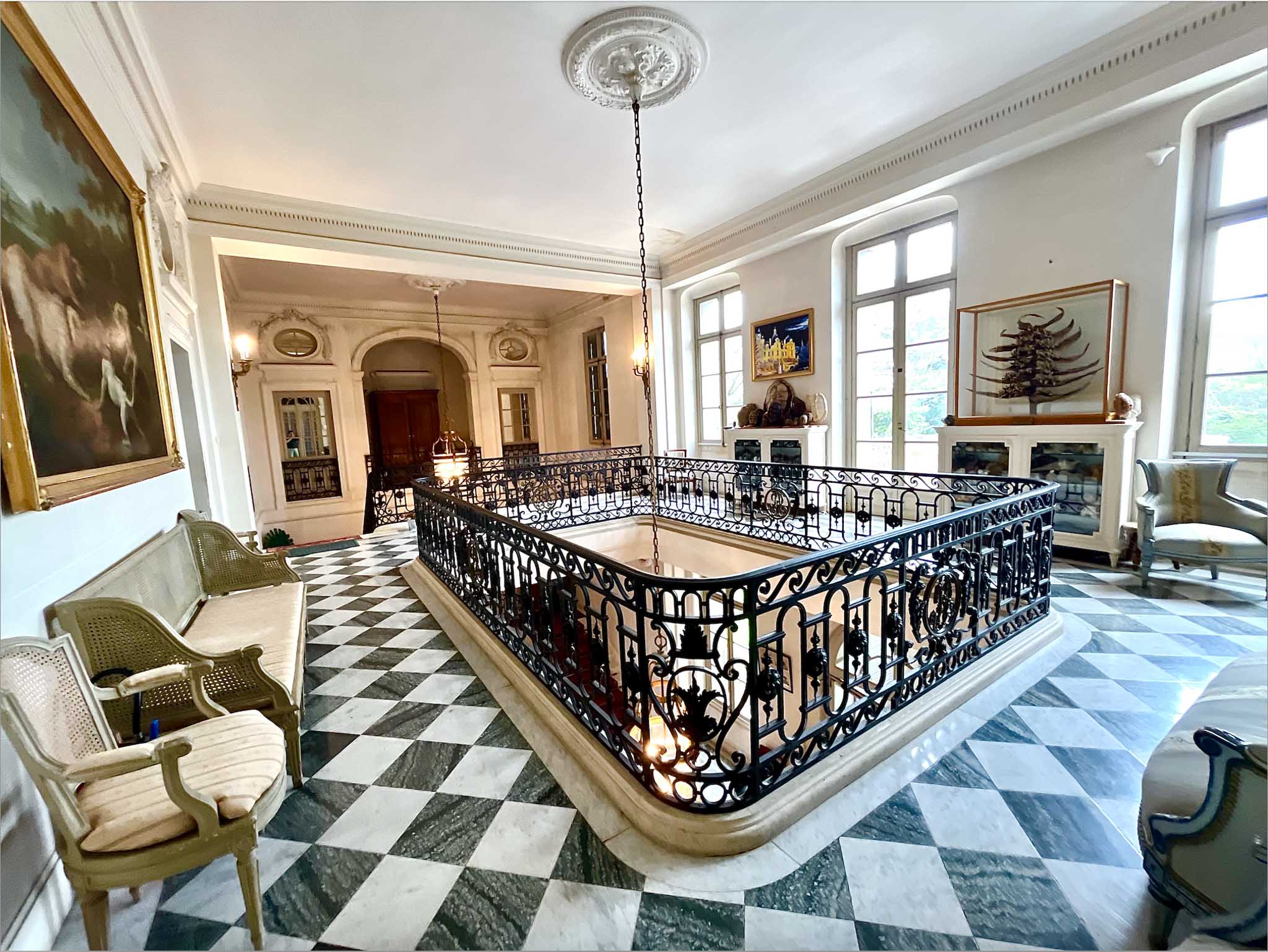 Grand chateau staircase hall with wrought-iron balustrade, black and white marble floor, and gilt-framed paintings